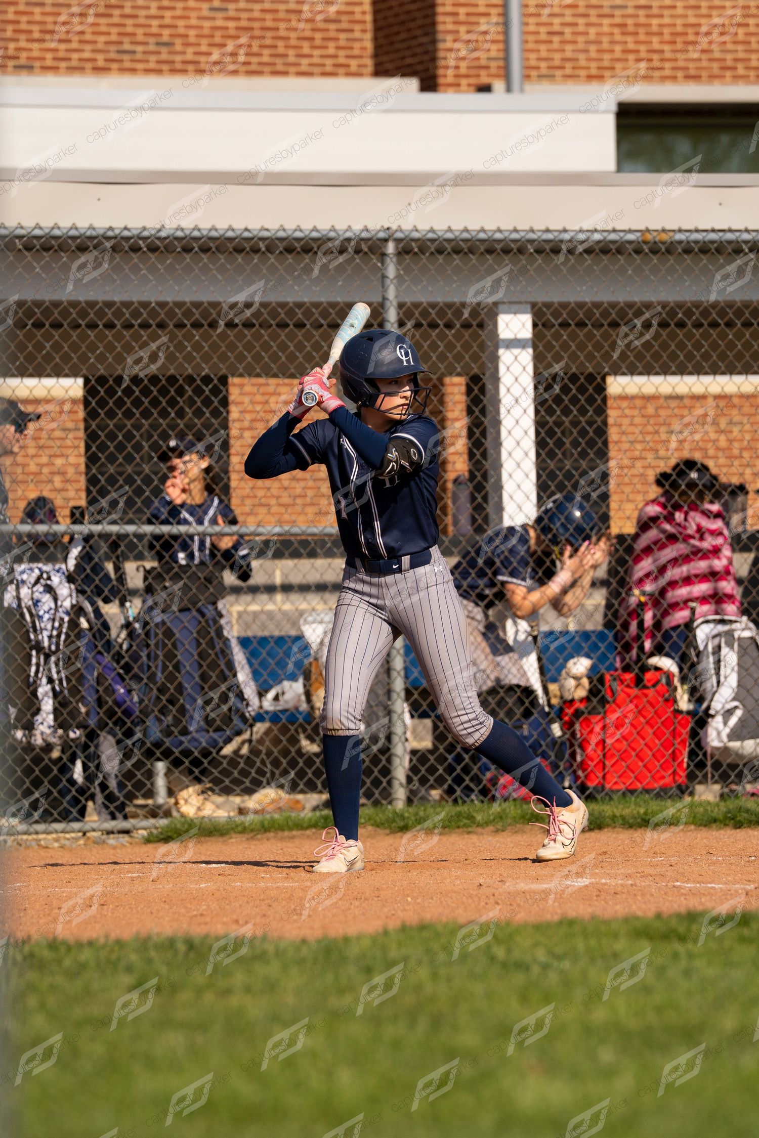 Female softball player in navy uniform standing in batting stance at home plate during a game.