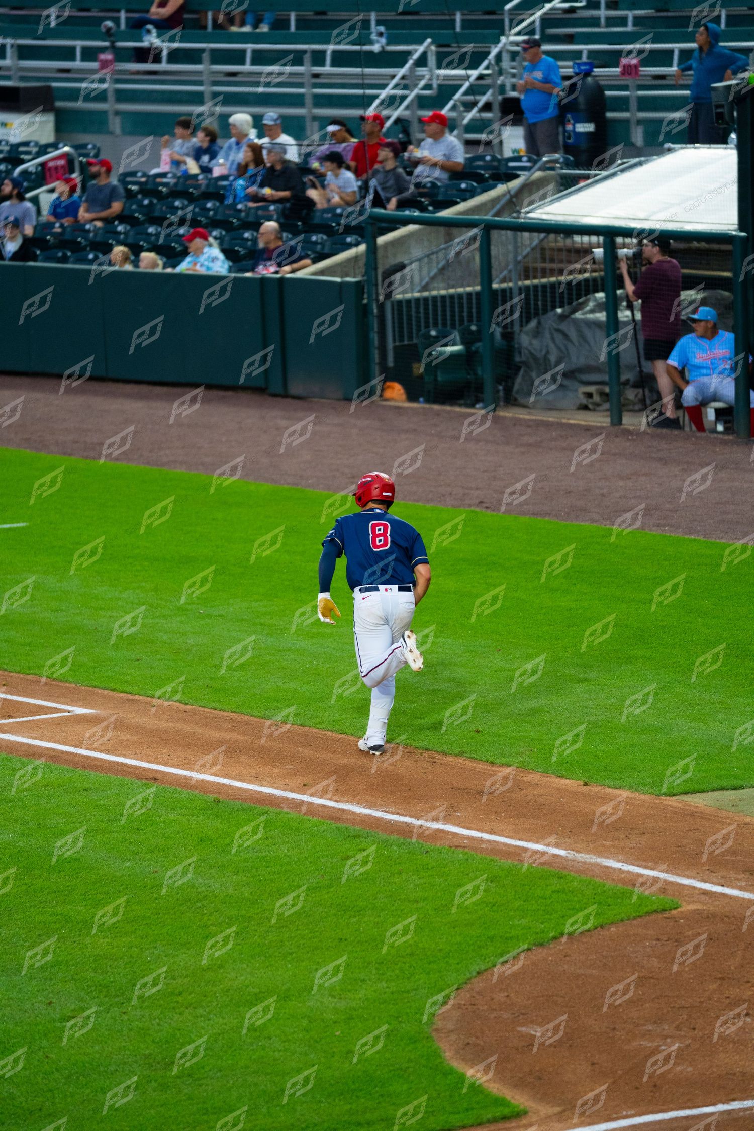Baseball player wearing number 8 in navy uniform runs along baseline toward home plate during game.