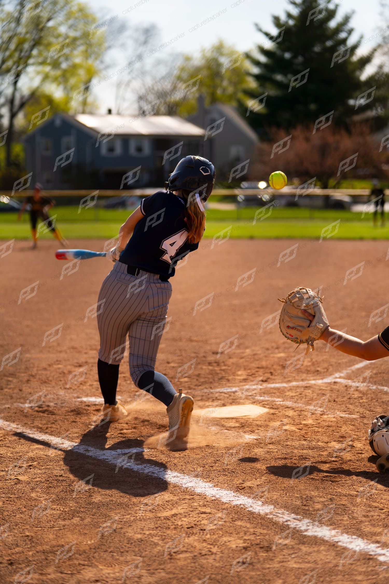 Softball player number 4 runs from home plate as catcher receives pitch during outdoor game.