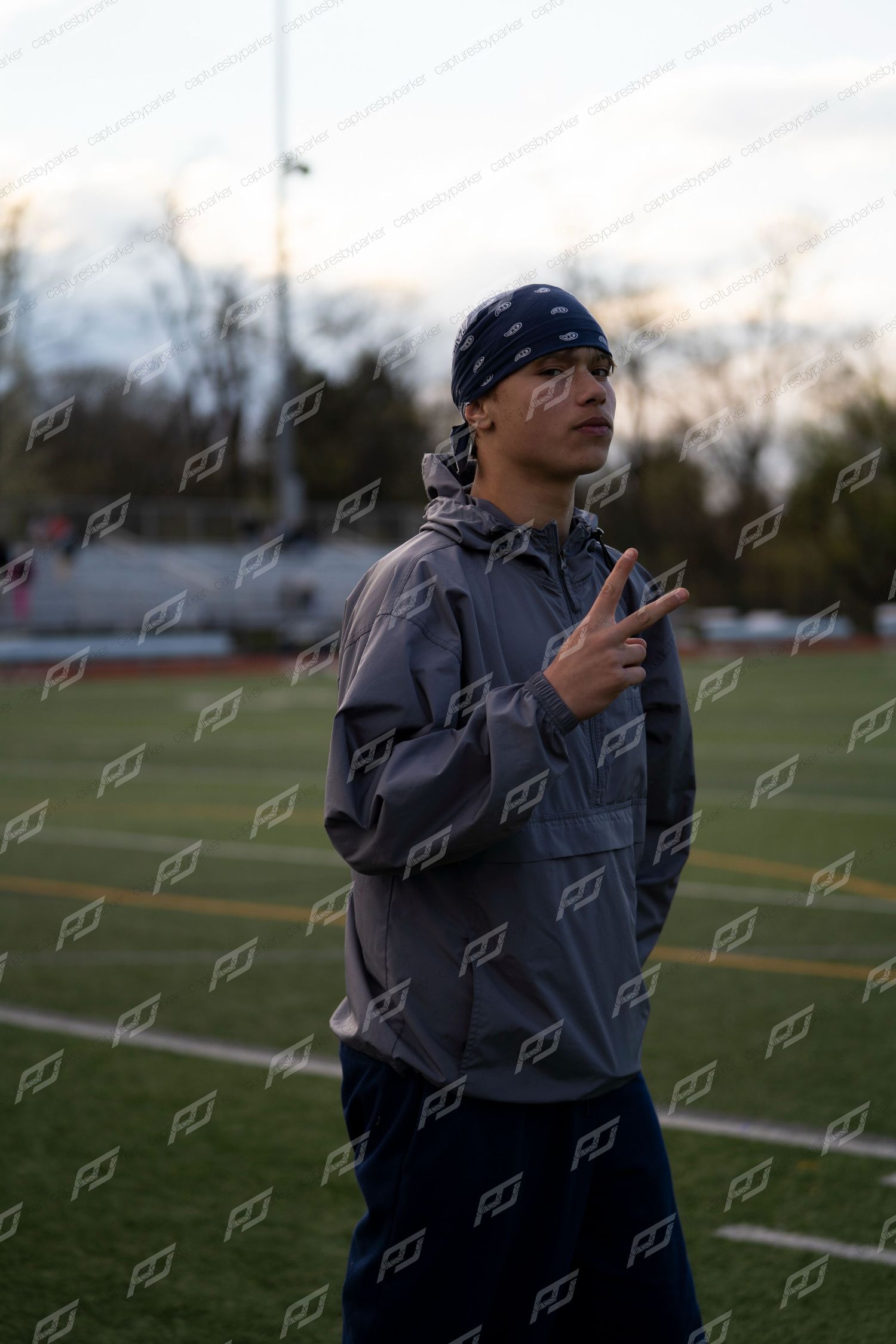 Young male athlete in gray jacket and bandana gestures on green field at track meet.