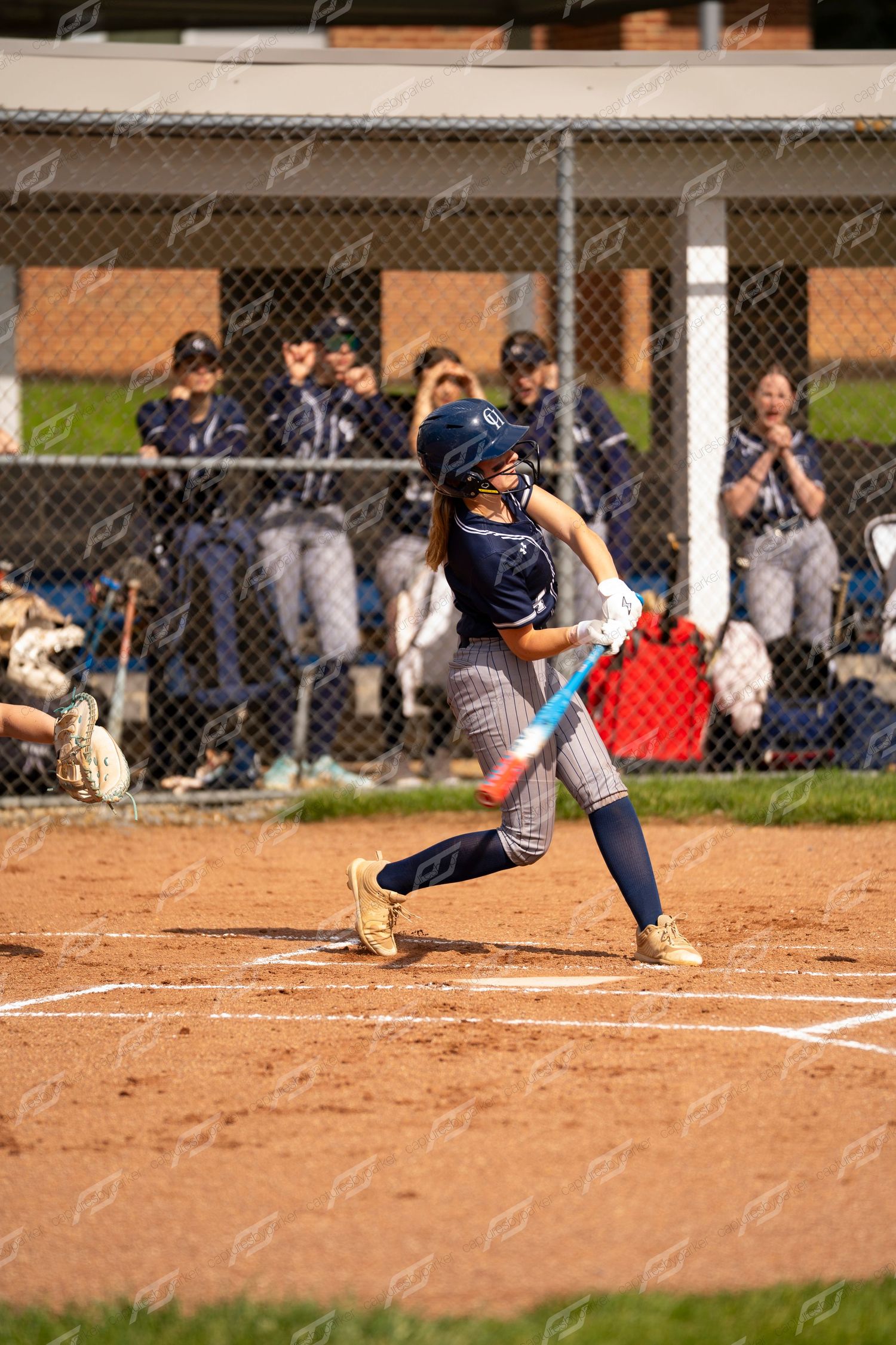Female softball player follows through on powerful swing during game.