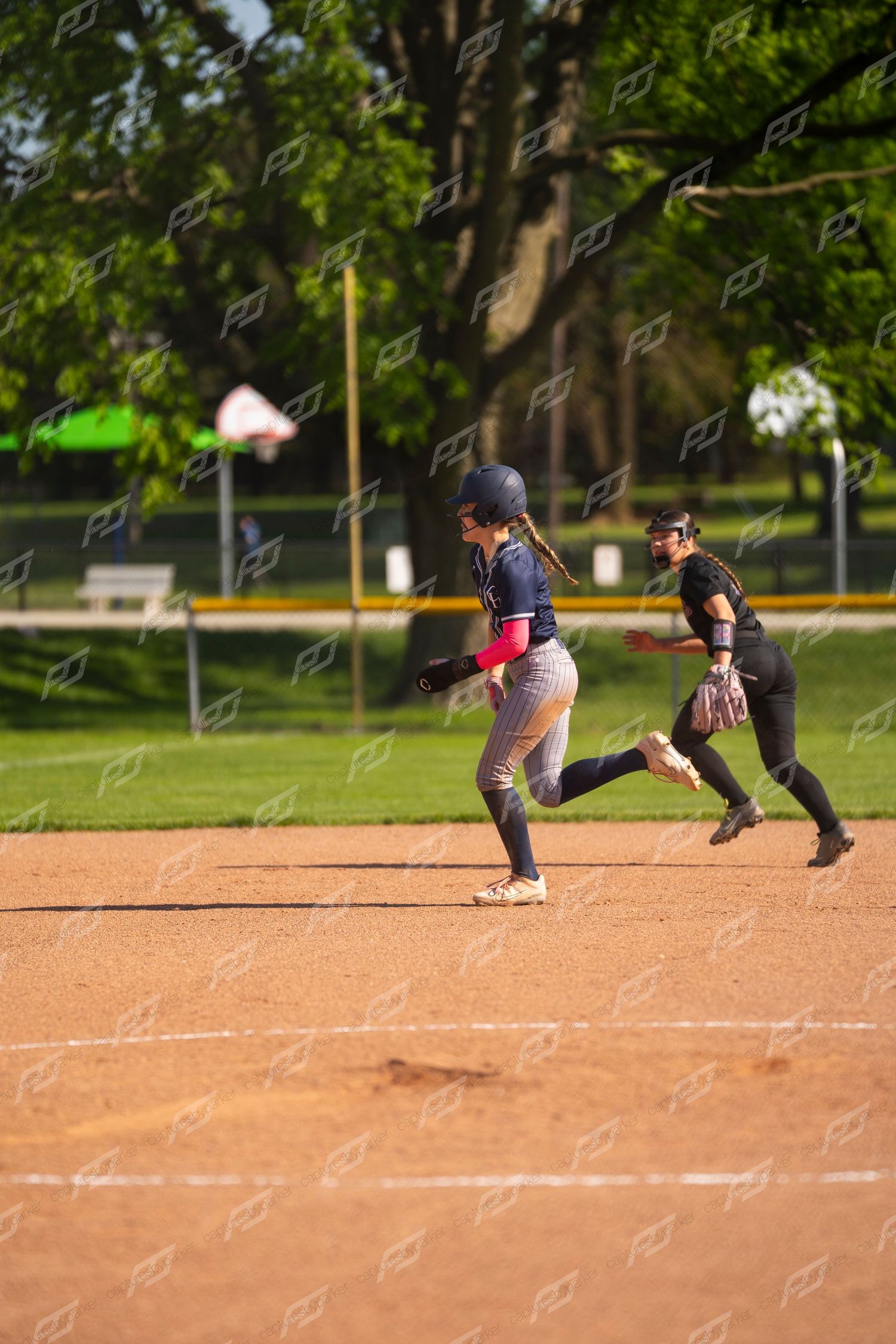 Softball player runs the bases as opposing first baseman prepares to make a play.