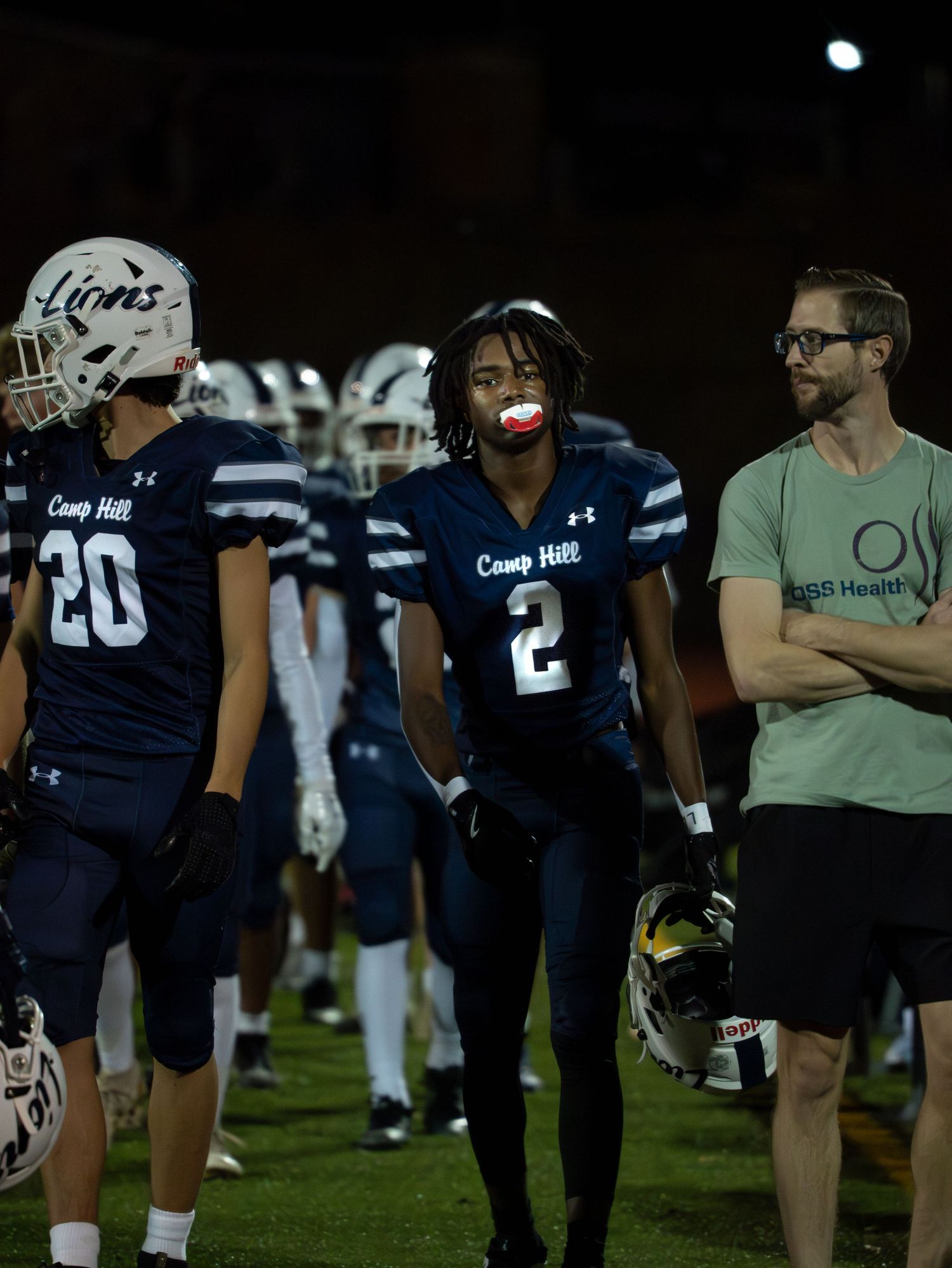 Camp Hill Lions player number 2 with red mouthguard walks sideline during a night football game.