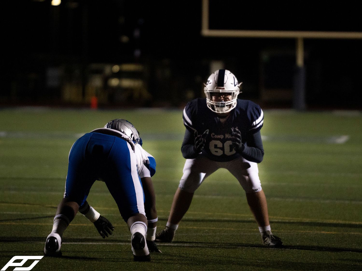 Football player number 60 lines up in defensive stance during night game.