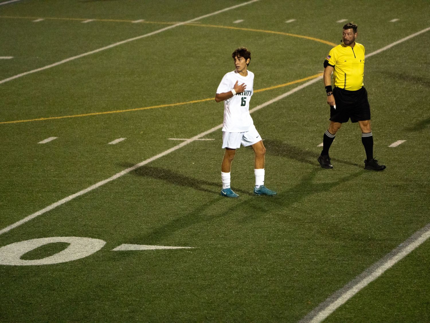 Soccer player number 6 in white uniform stands near referee in yellow on turf field.