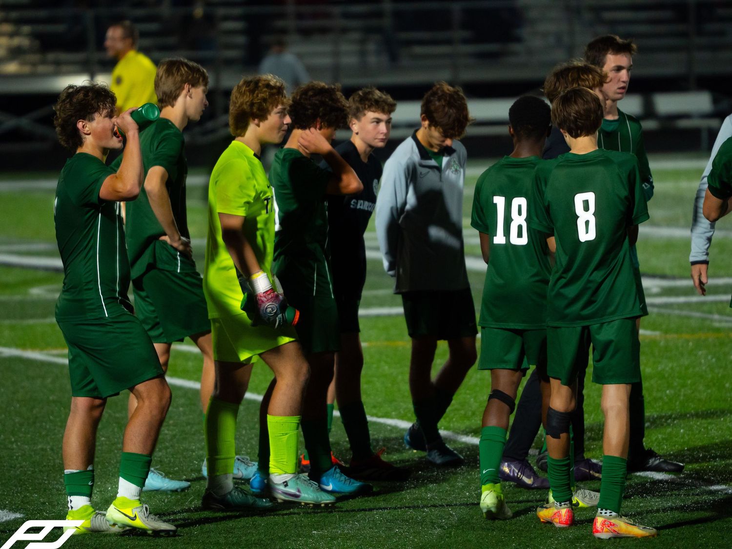 Trinity soccer team in green uniforms gathered on the turf field during a night game.