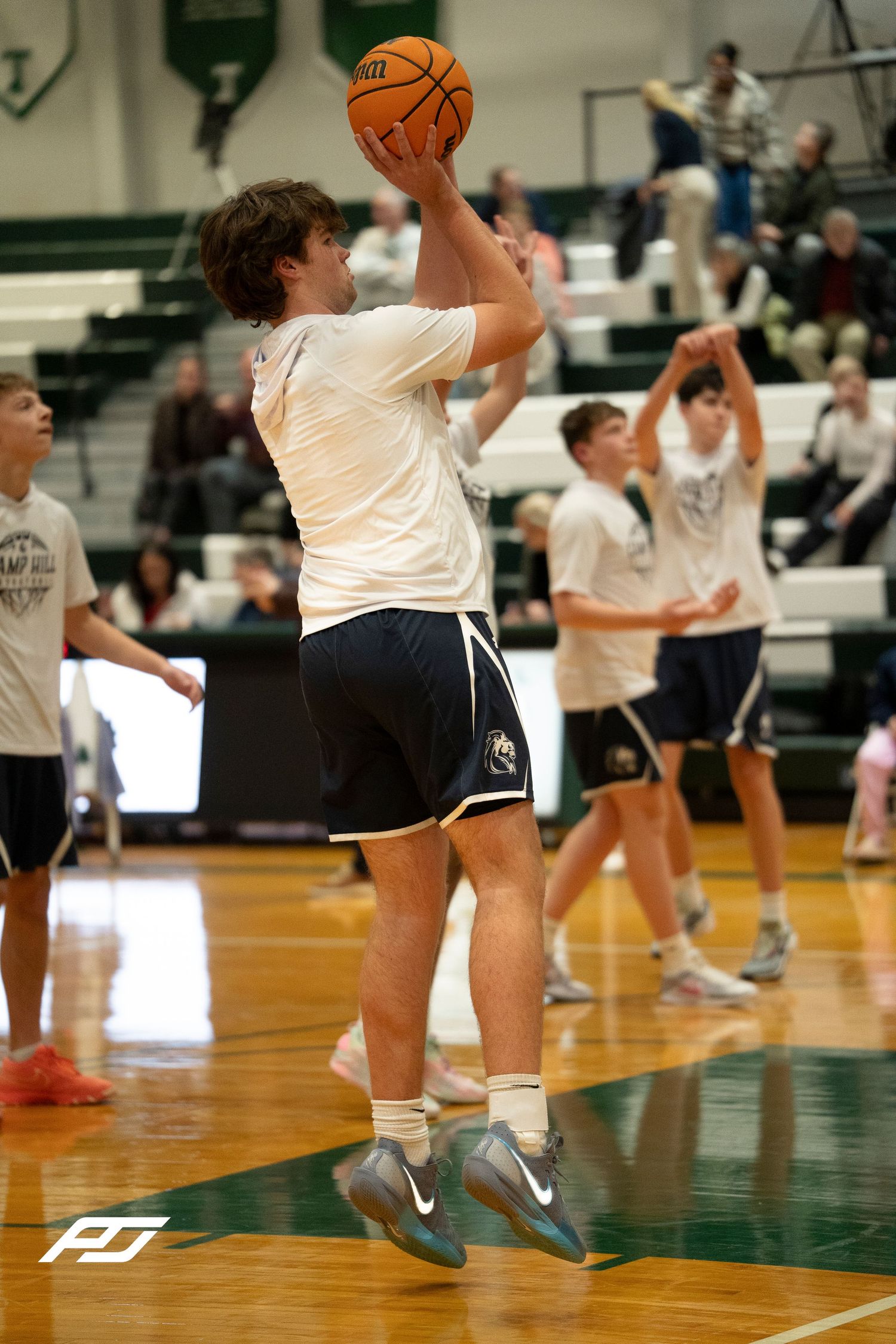 High school basketball player in white warmup uniform jumps to shoot during pre-game warmup drills.