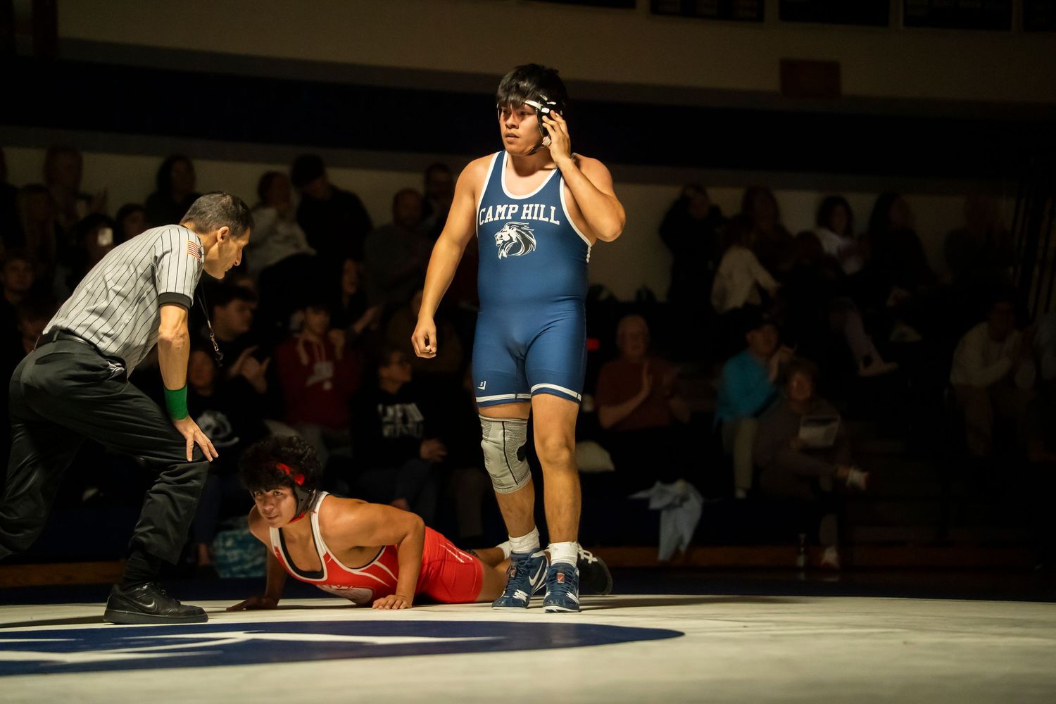 Camp Hill wrestler in blue singlet stands victorious over fallen opponent in red during high school wrestling meet.