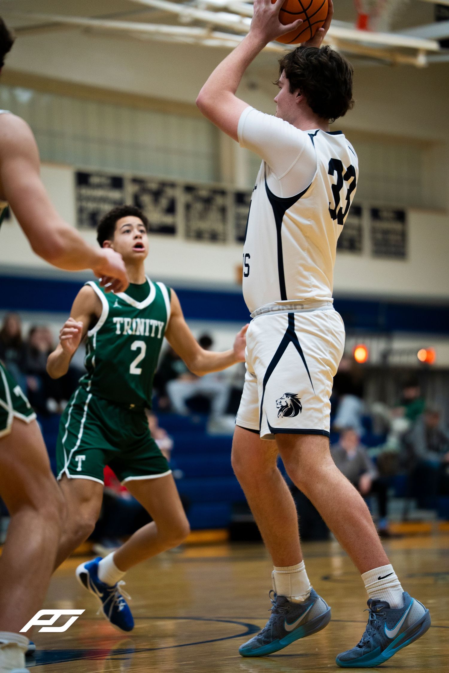 Player #33 in white uniform shoots basketball over Trinity defender #2 in green during high school game.