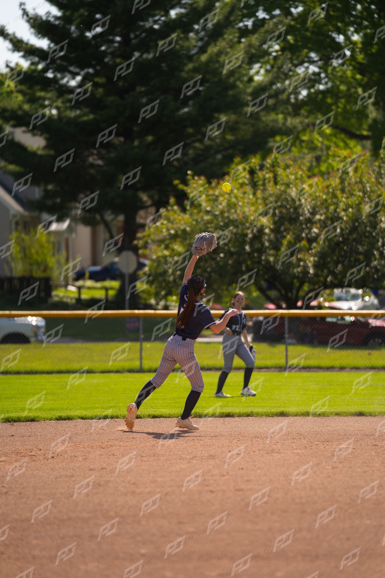 Softball infielder stretches to catch a fly ball during an outdoor game on a sunny day.