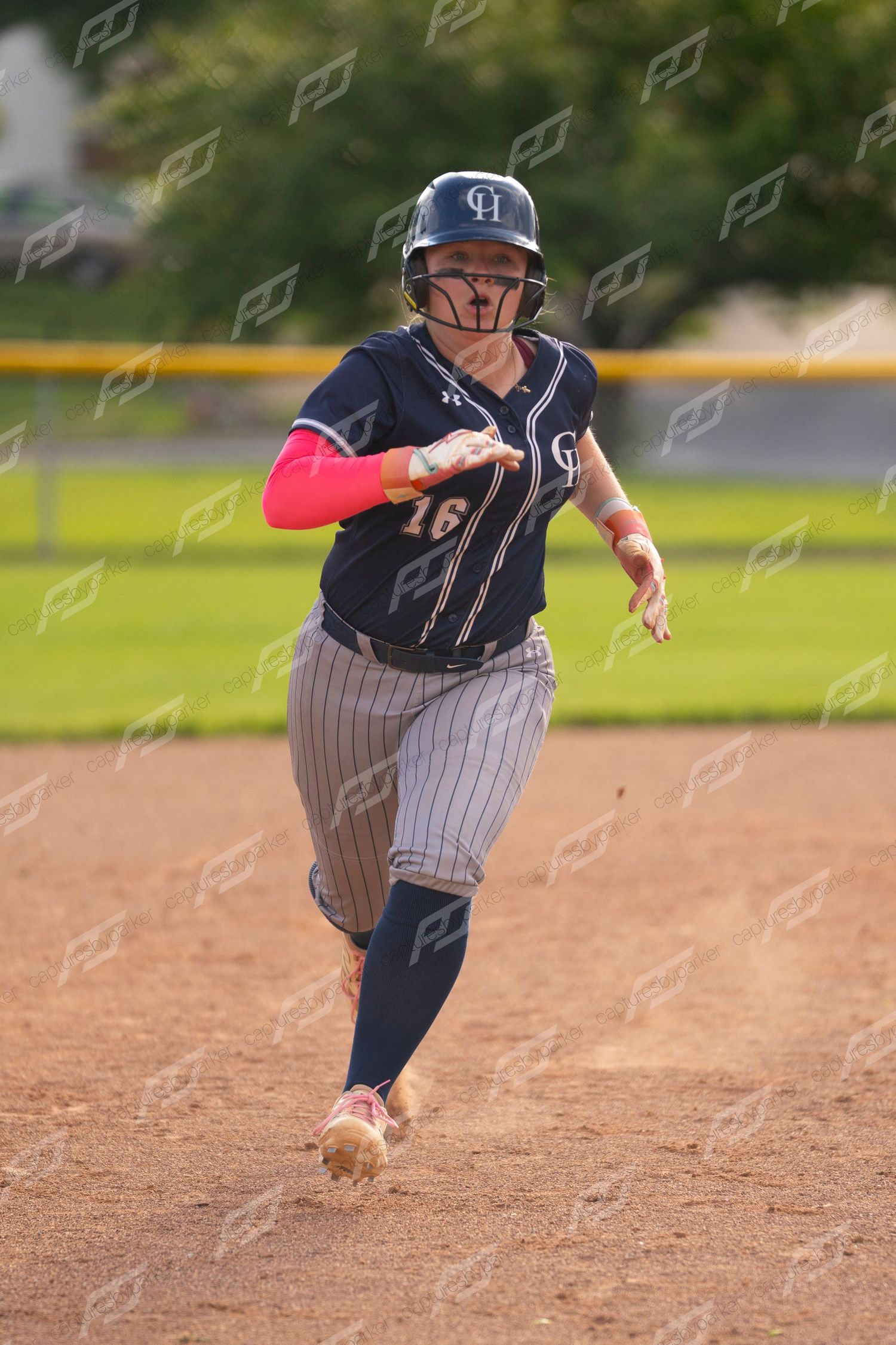 Softball player #16 in navy uniform with pink sleeves sprinting around second base.