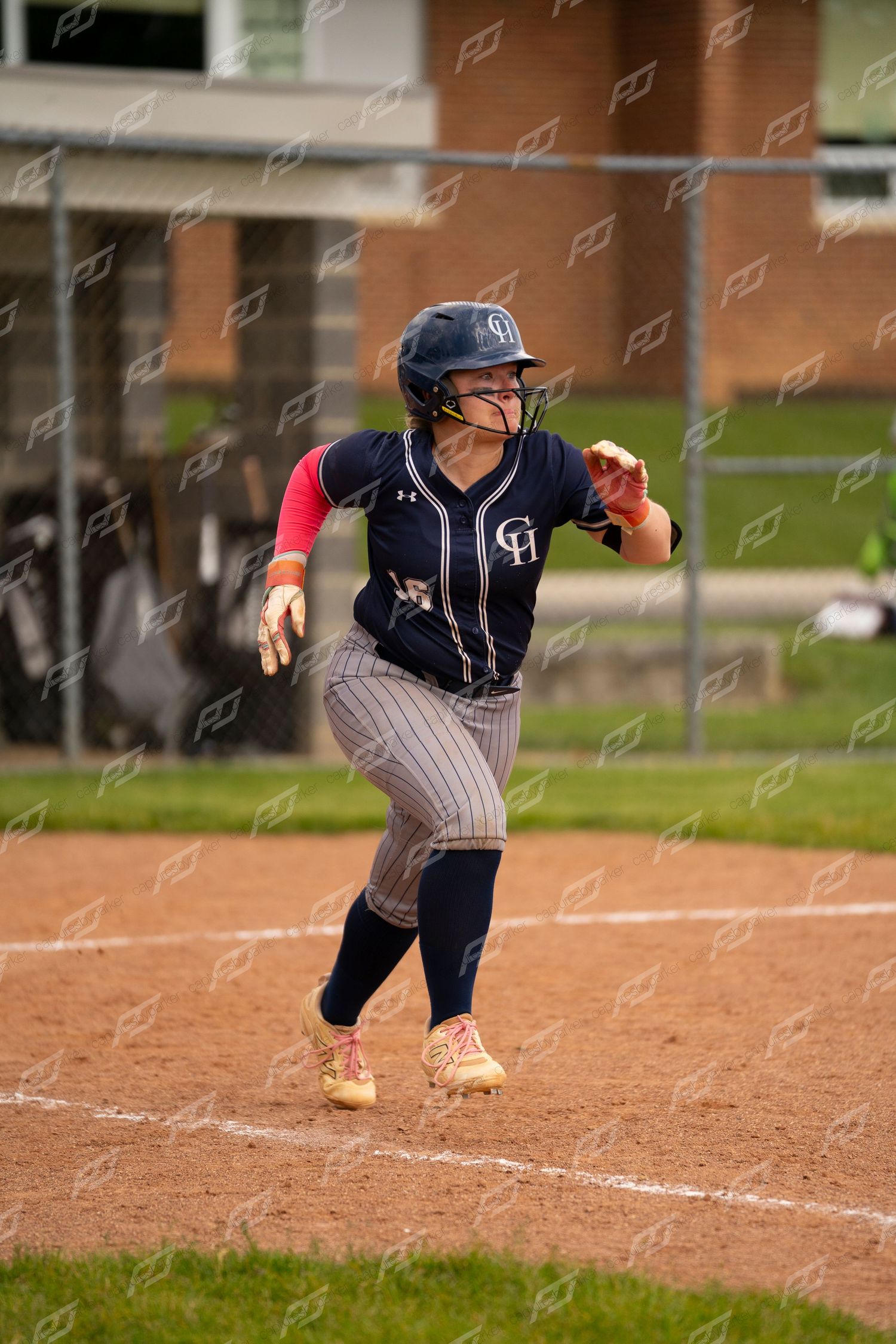 Female softball player in navy Under Armour uniform sprints toward first base.