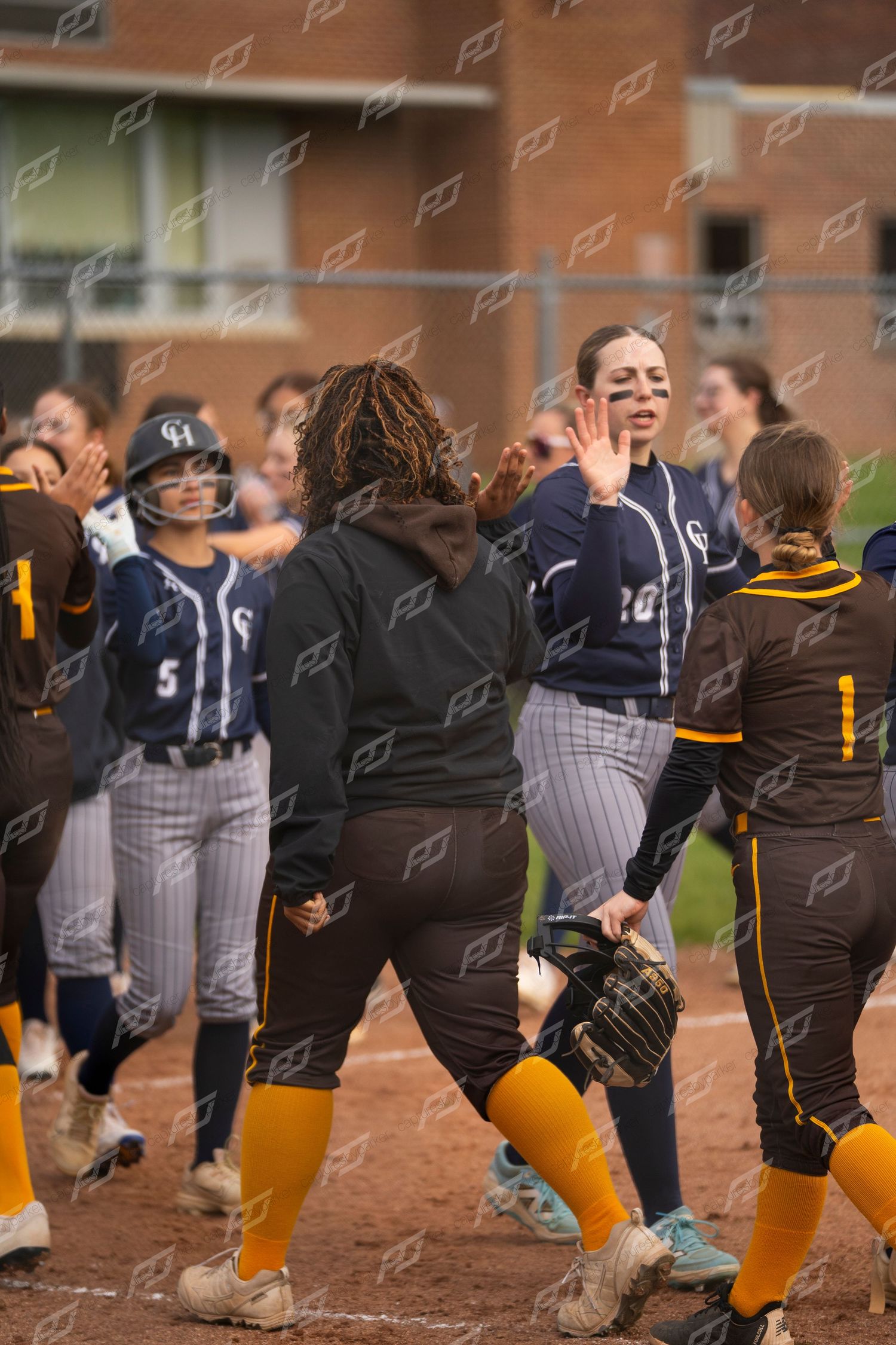 Softball teams exchange high-fives in a post-game handshake line after the match.