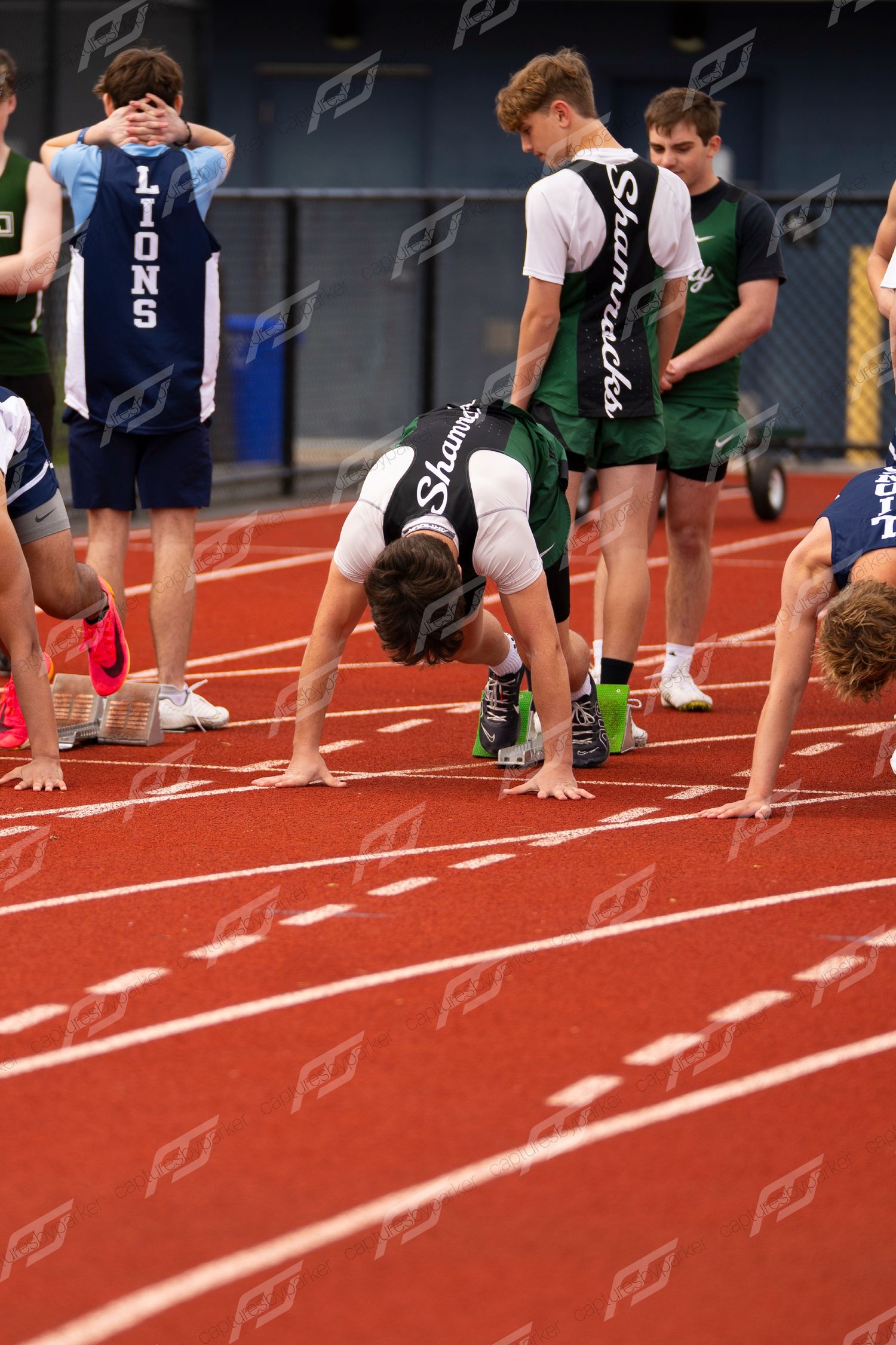 High school sprinters crouch in starting position on red track at Kunkel Field House invitational meet.