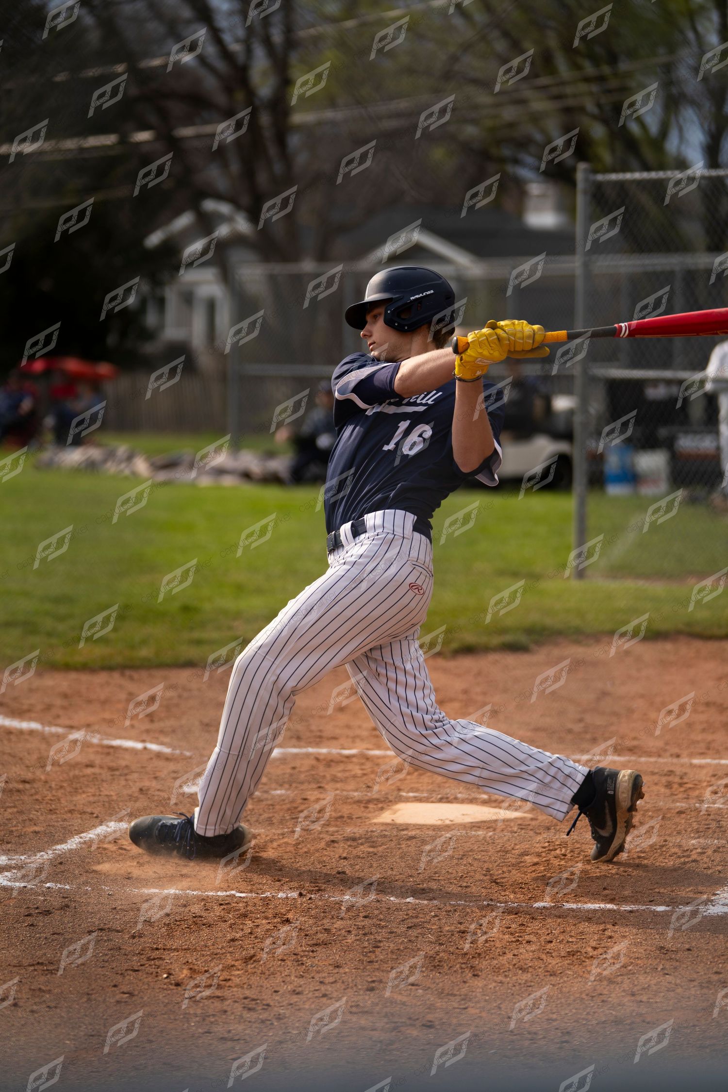 Baseball player #16 in navy pinstripe uniform completes a full bat swing at plate.