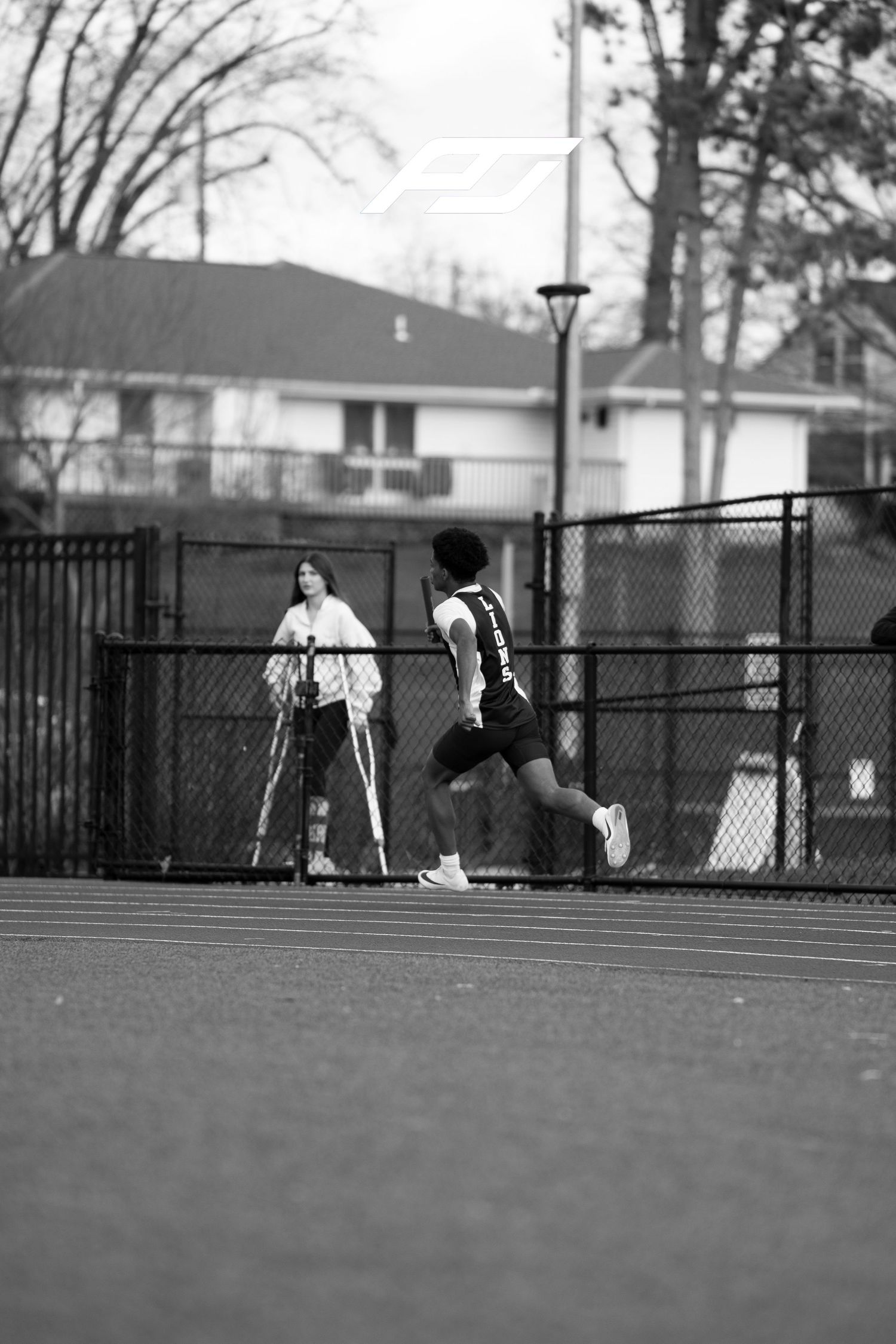 Young track athlete sprints past spectator on outdoor running track during competition.
