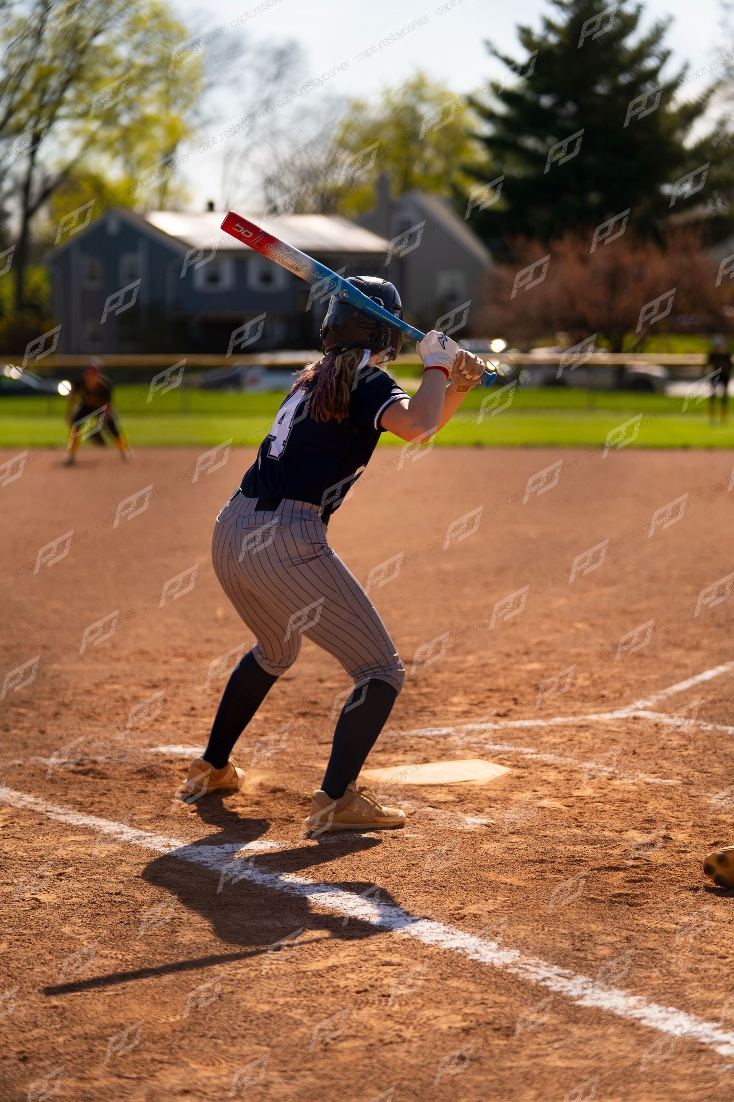 Softball player in navy uniform winds up to bat at home plate during an outdoor game on a sunny day.