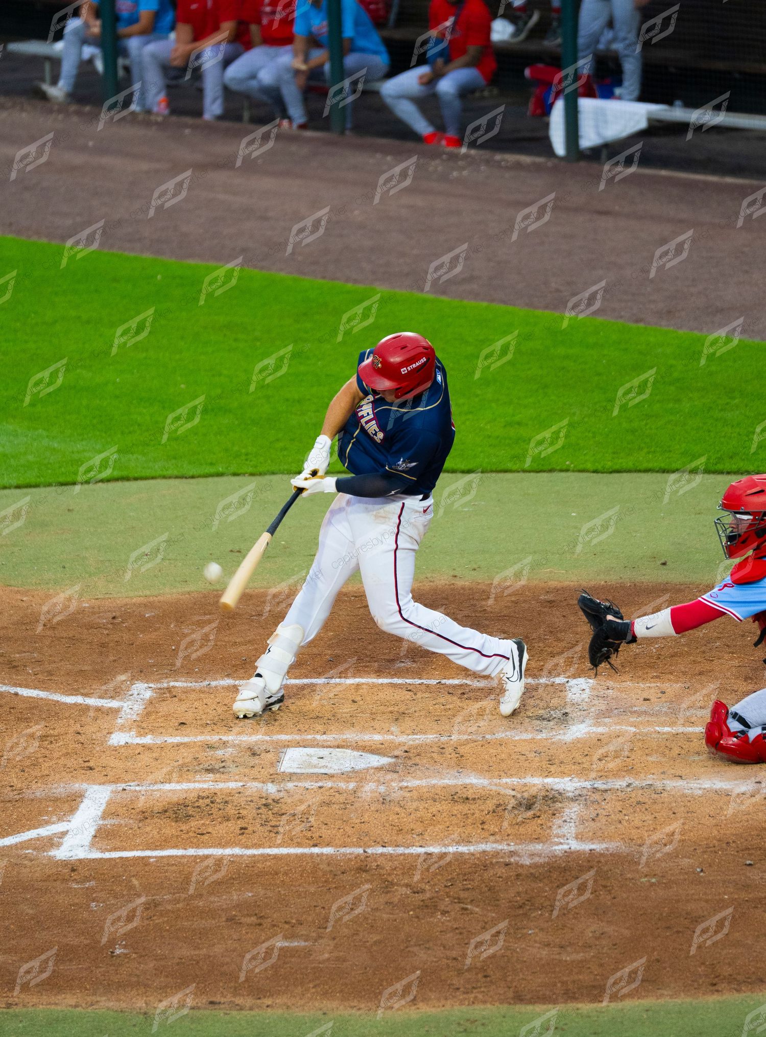 Baseball batter in navy uniform makes contact with pitch as catcher crouches behind home plate during game.