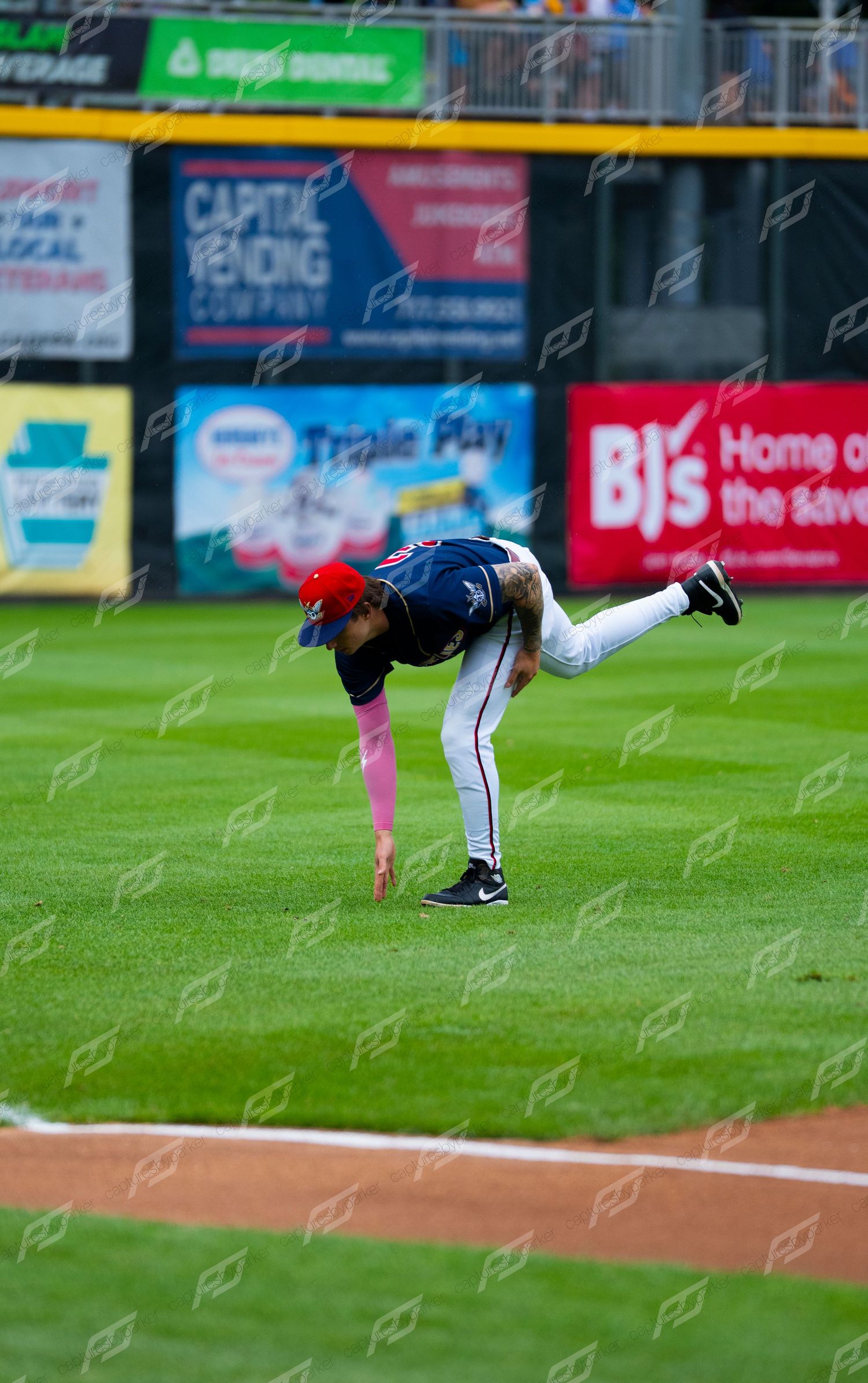 Baseball player bending down to field a ball on a green grass outfield during a minor league game.