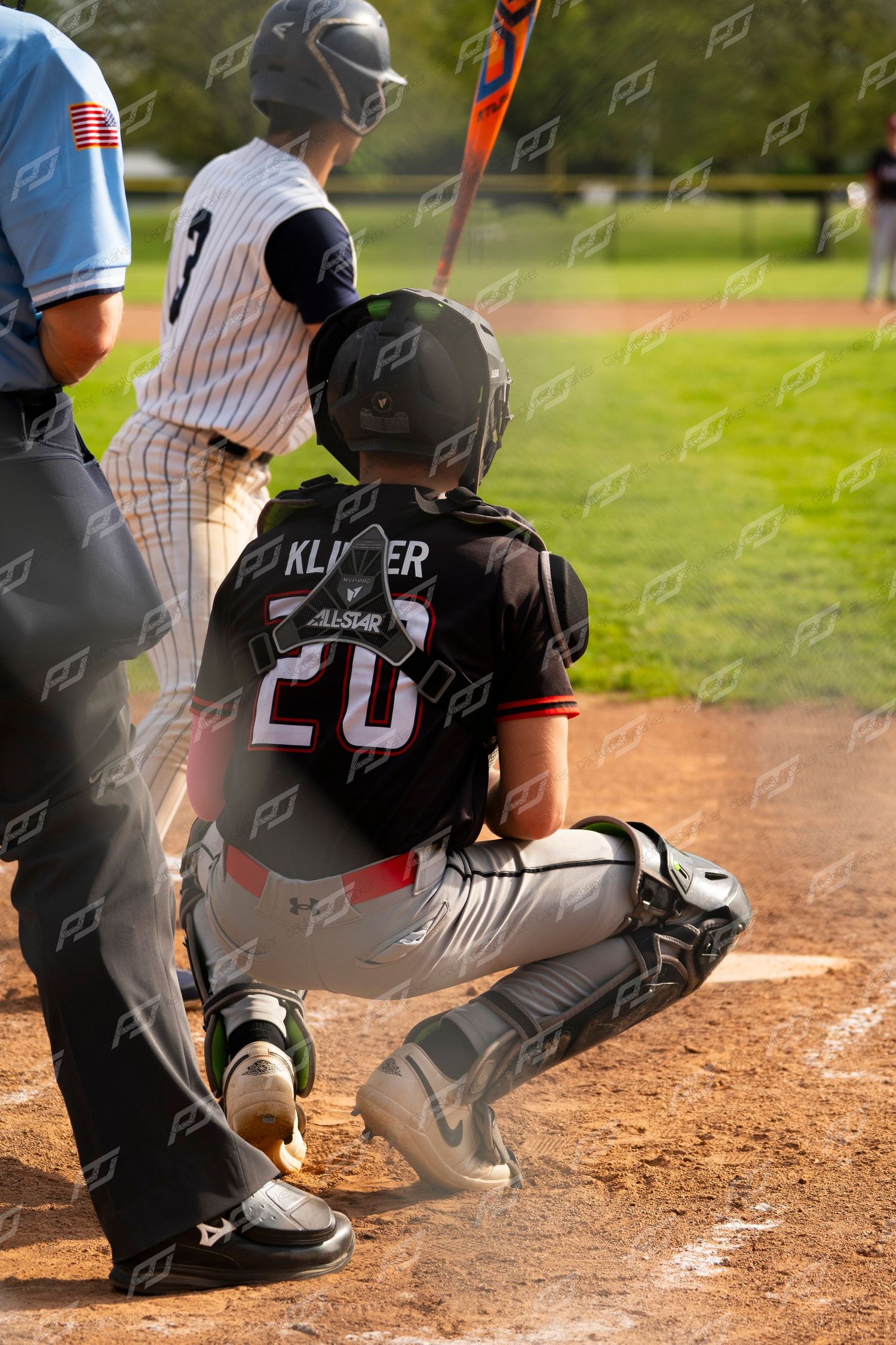 Baseball catcher number 20 Klinger crouches behind home plate in full gear during a youth baseball game.