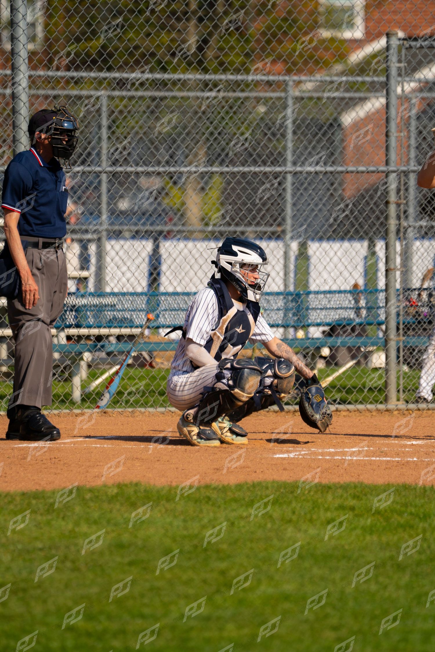 Baseball catcher in full gear crouches at home plate with umpire standing behind during a game.