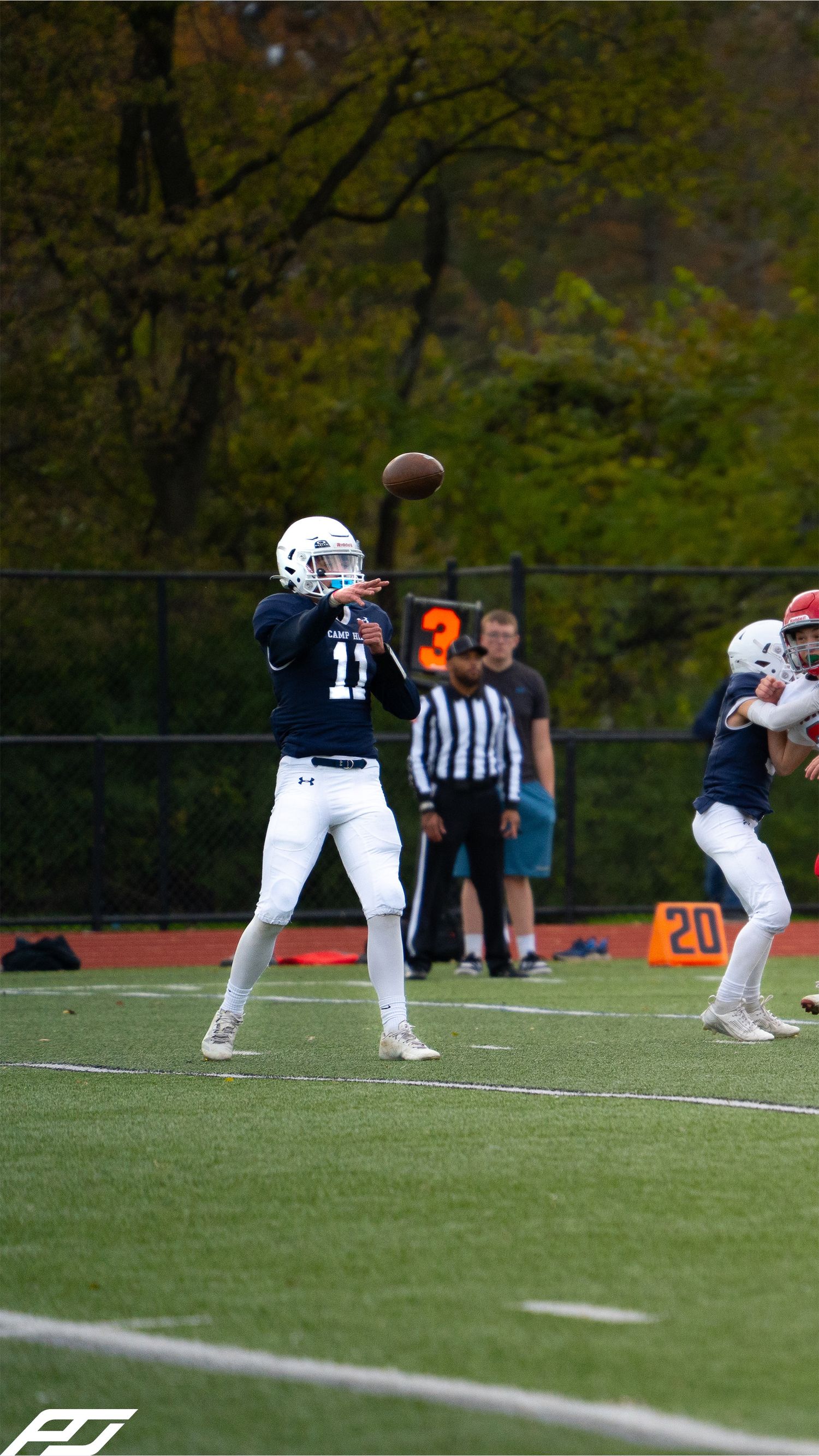 Youth football quarterback number 11 in navy uniform throws a pass during an autumn turf field game.