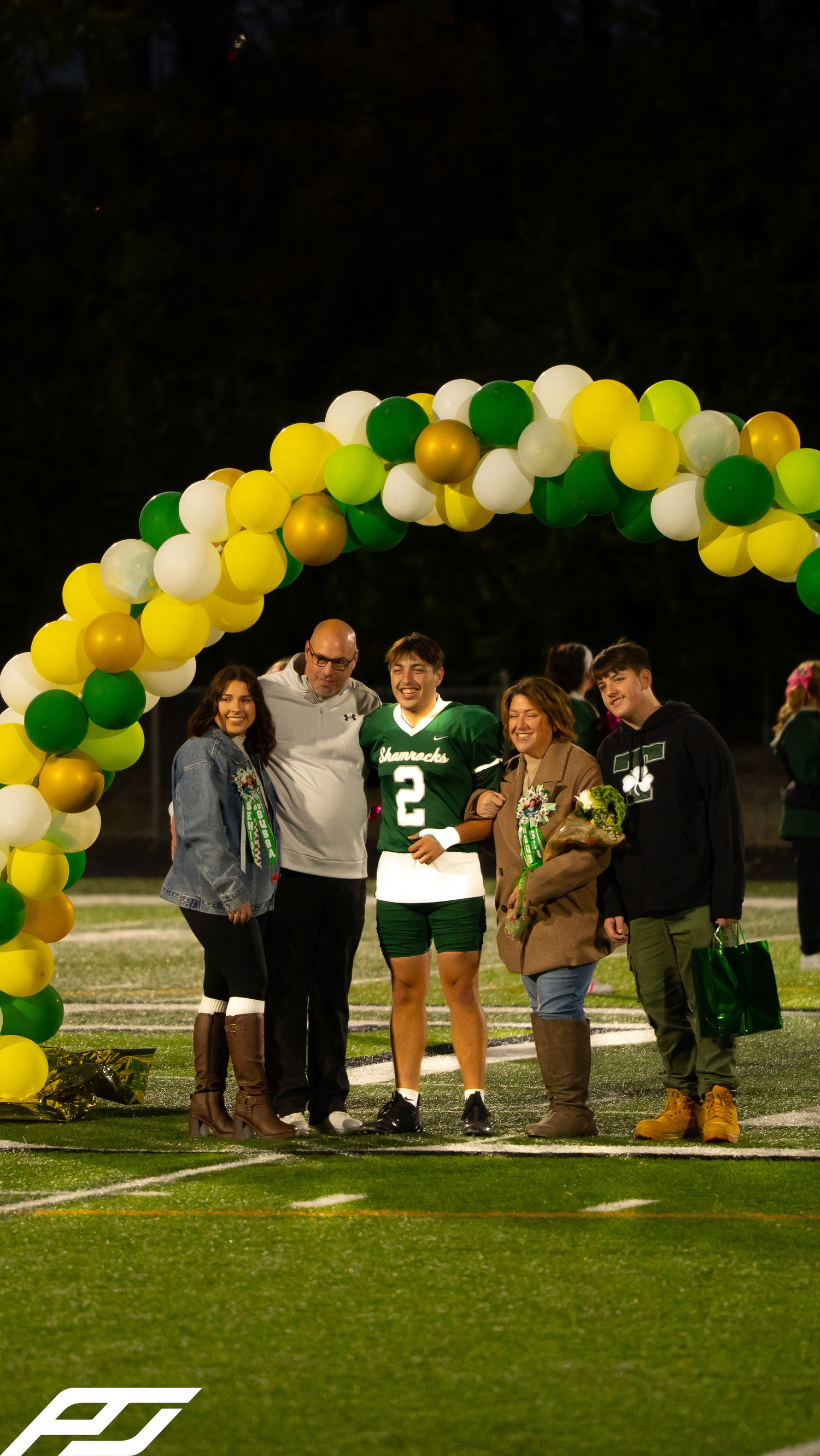 Football player in green jersey poses with four family members under a green and yellow balloon arch.