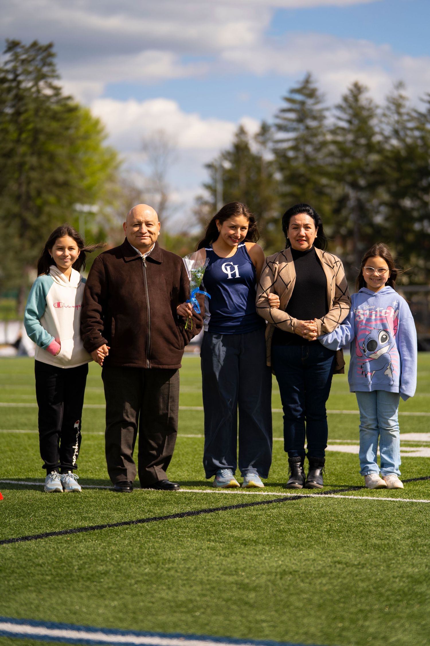 A family of five poses on a football field during a school senior day ceremony.
