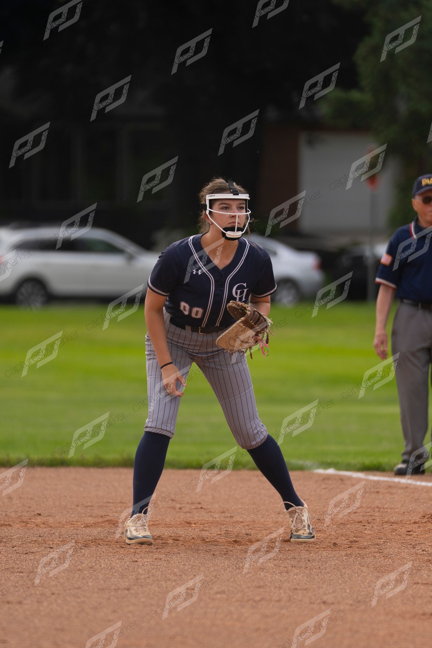 Female softball infielder in navy pinstripe uniform crouches in ready position near a base.