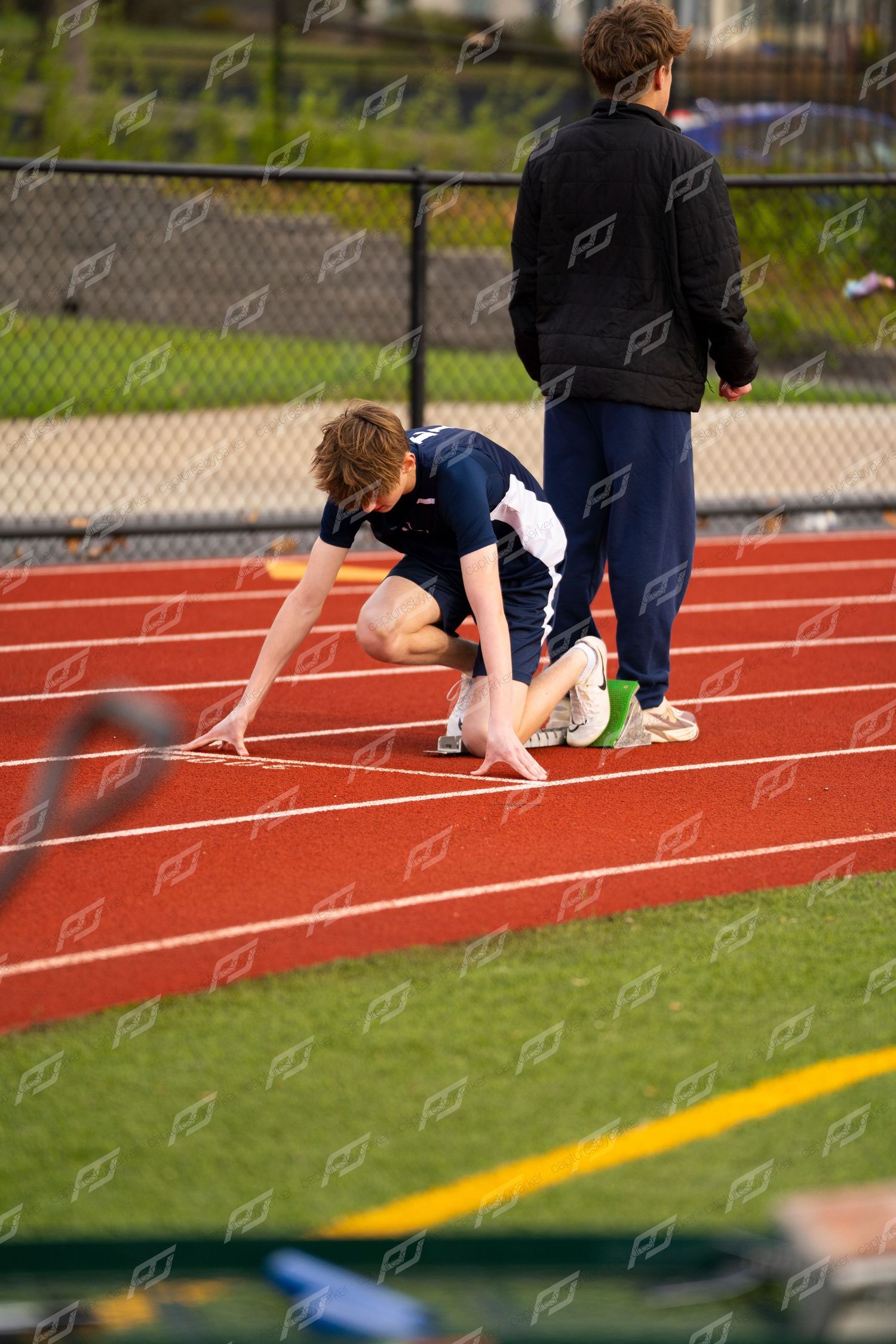 High school track athlete crouching in starting blocks on red running track.