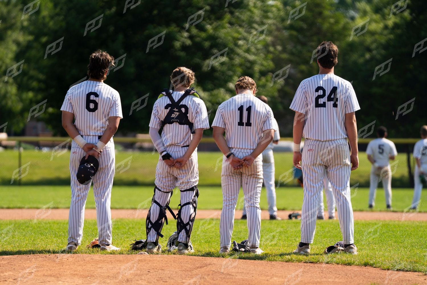 Four baseball players in pinstripe uniforms standing together on the field including a catcher in gear.
