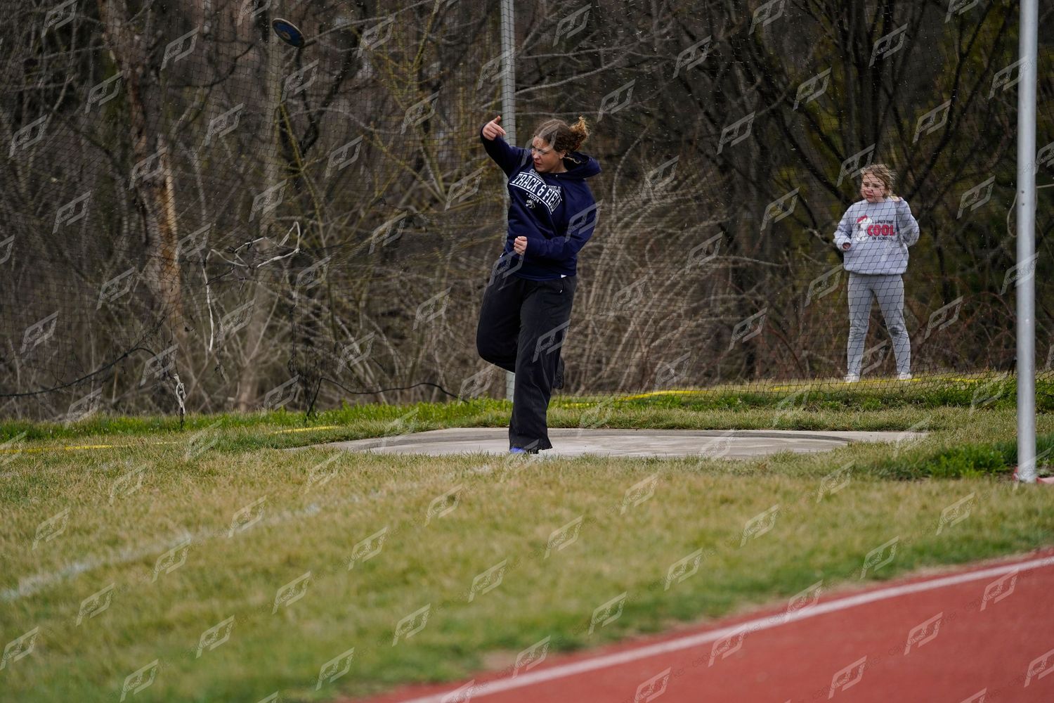 Female athlete in navy uniform throws a discus at an outdoor high school track and field meet.