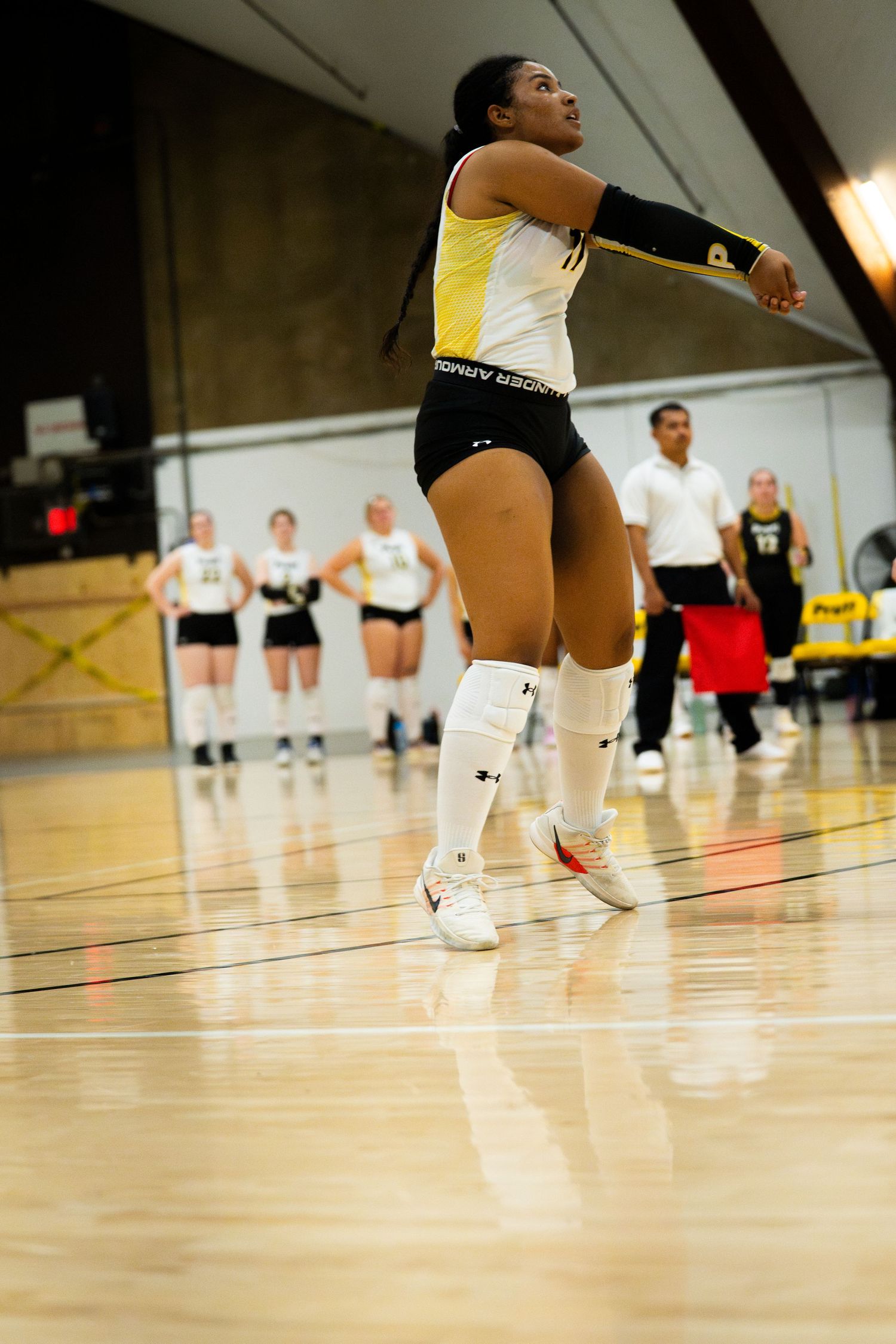 Female volleyball player jumps to hit ball during indoor collegiate volleyball game.