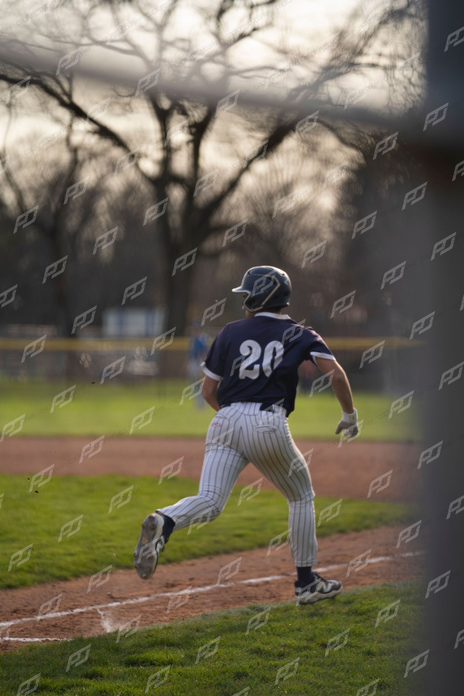 Baseball player #20 sprints along the baseline during an outdoor game at dusk.