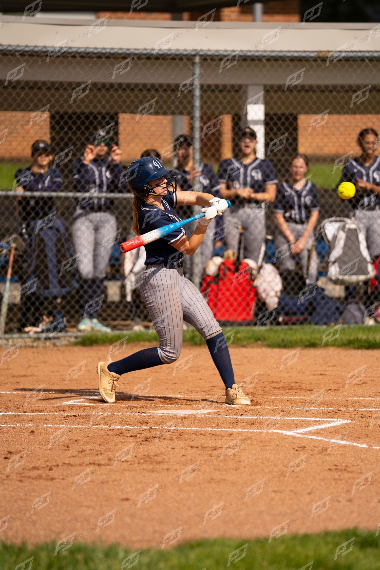 Softball player swings bat making contact with yellow ball during game.