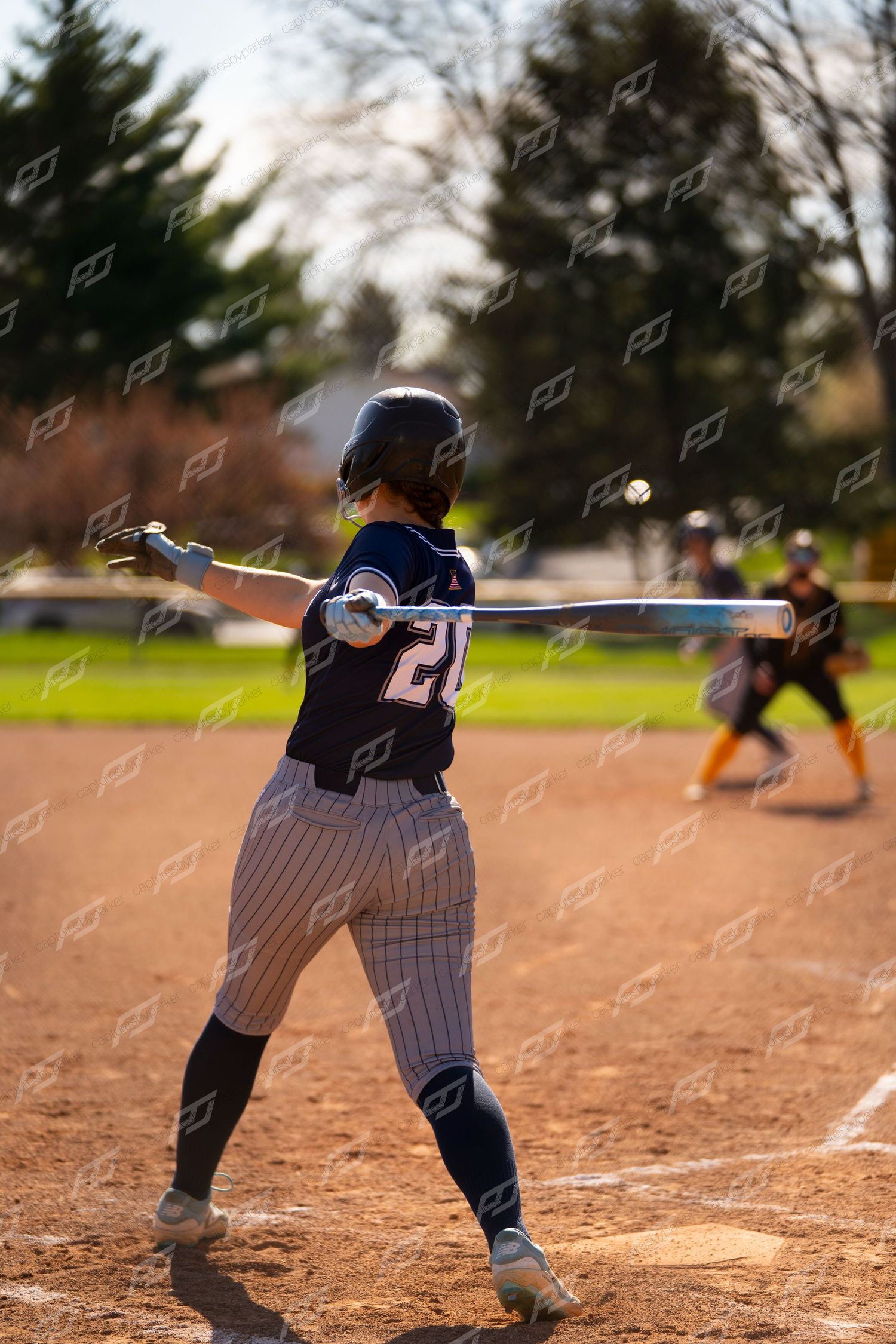 Softball player number 20 in navy pinstripe uniform winds up to swing bat during outdoor game.
