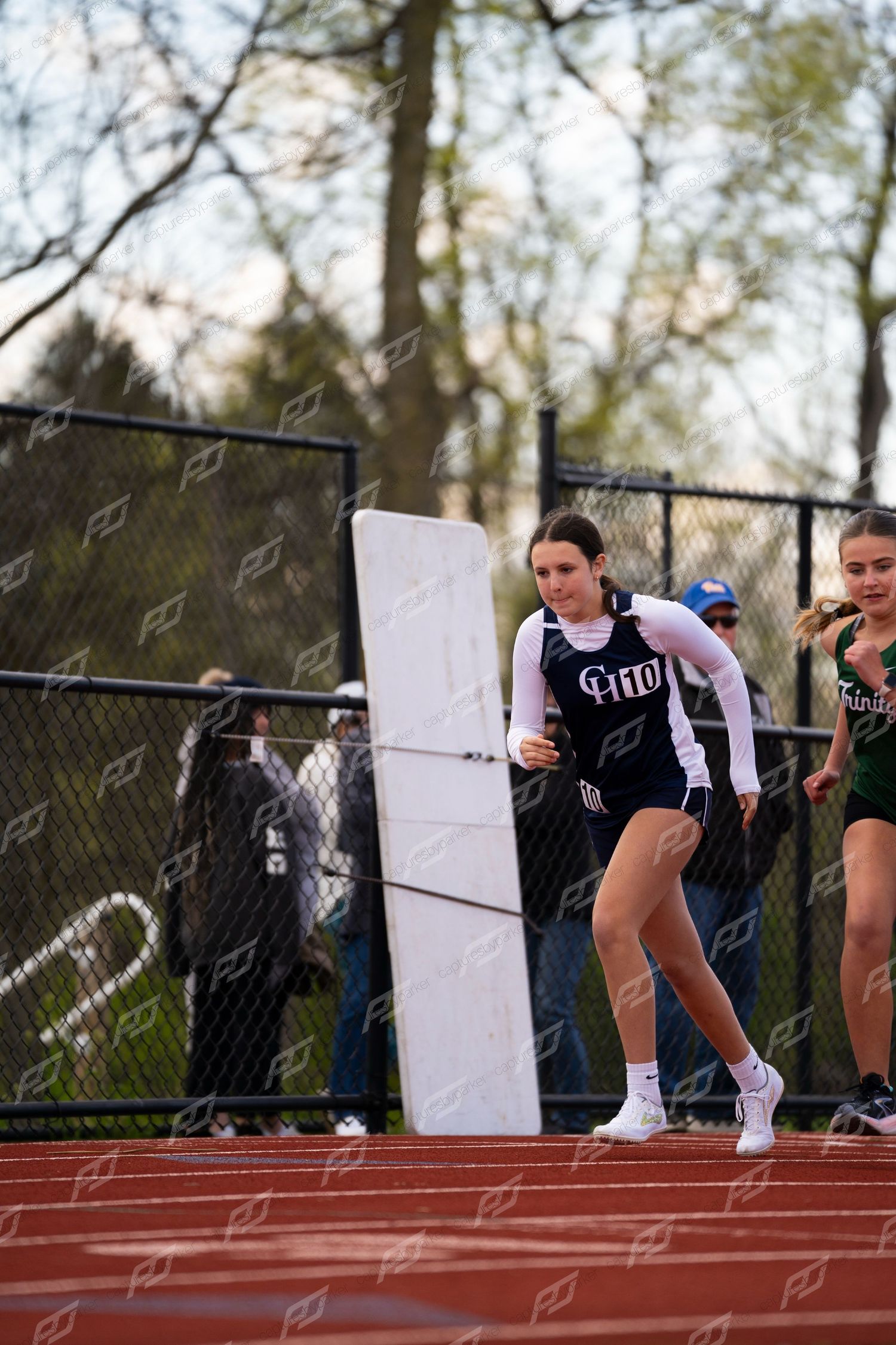 Female track athlete in black GH uniform rounds corner during outdoor high school track meet.