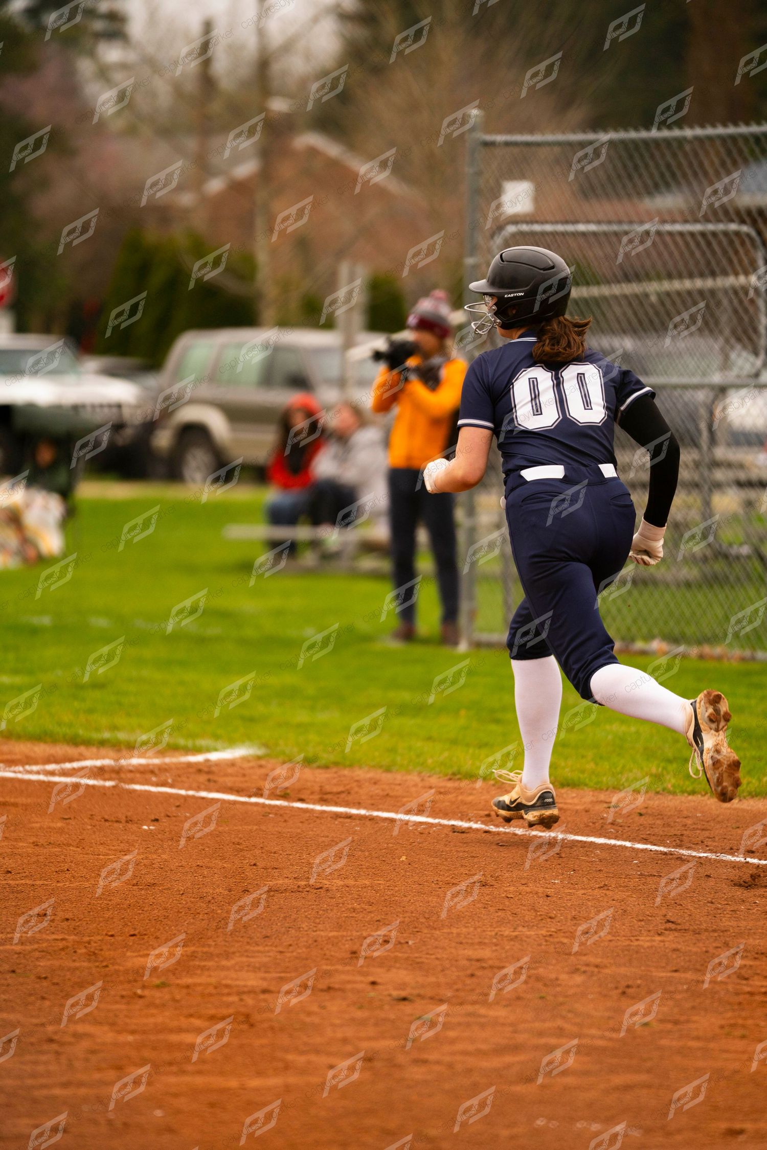 Female softball player #00 in navy uniform runs the baseline during an outdoor game.
