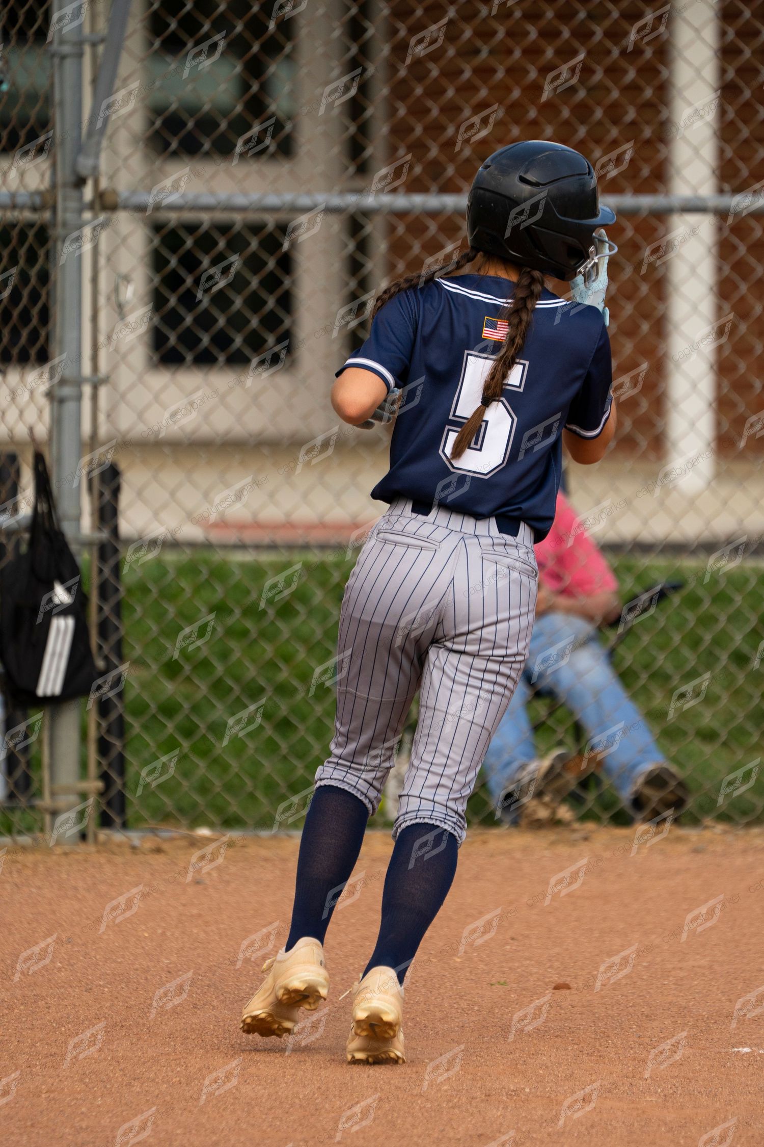 Female softball player number 5 in navy pinstripe uniform runs bases wearing gold cleats.