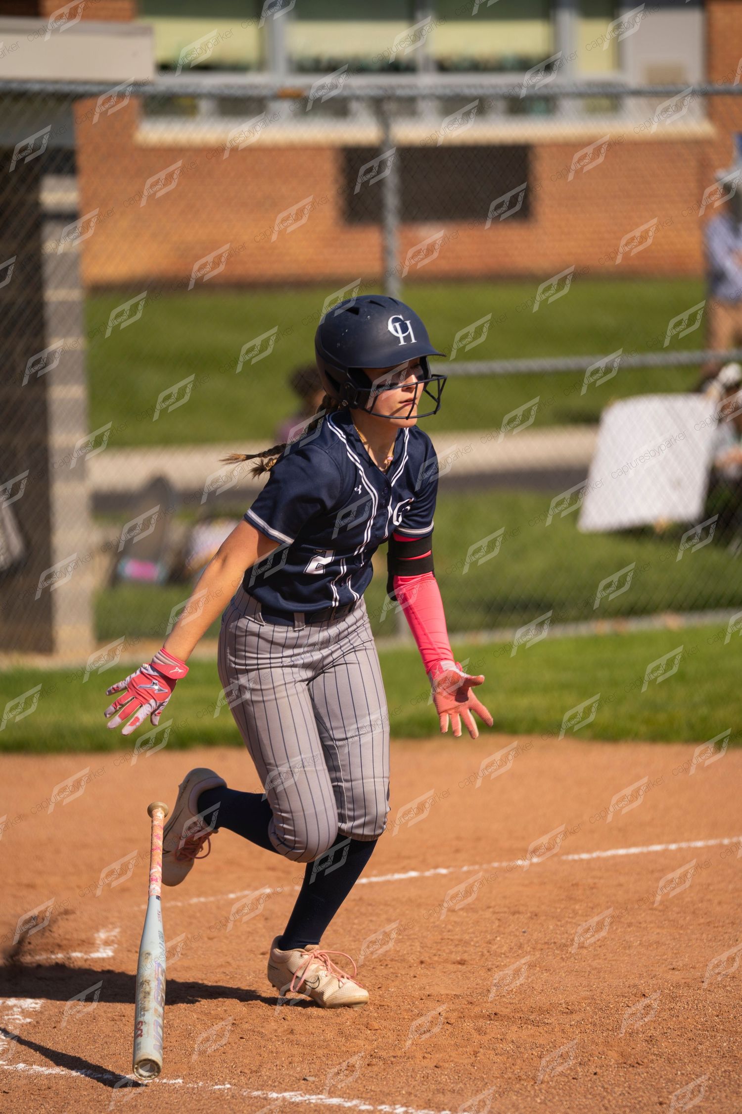 Female softball player sprints from home plate after making contact during a daytime game.