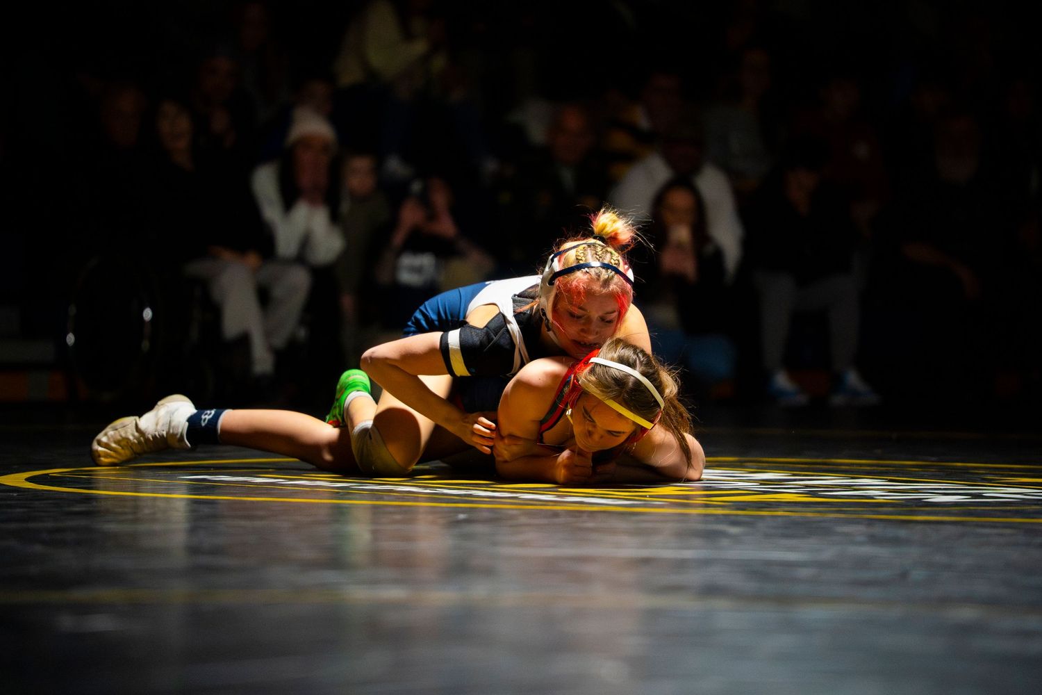 Female wrestler pins opponent to mat during intense competitive wrestling tournament match.