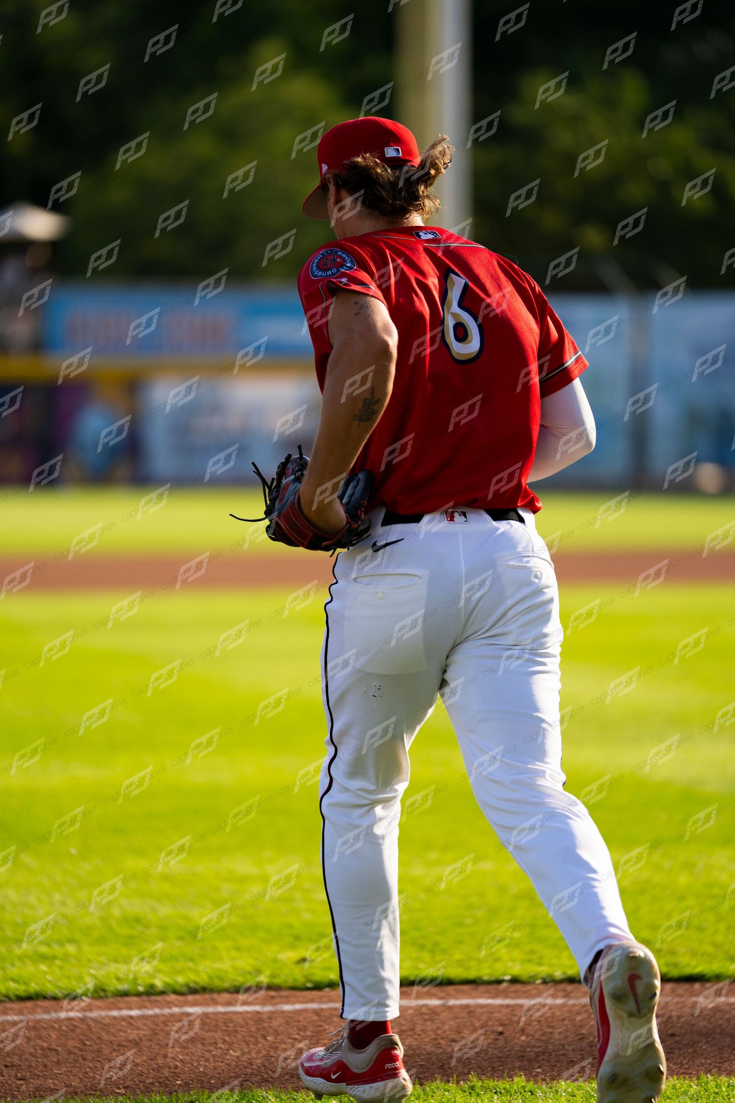Baseball pitcher wearing number 6 in red uniform prepares to deliver a pitch during a day game.