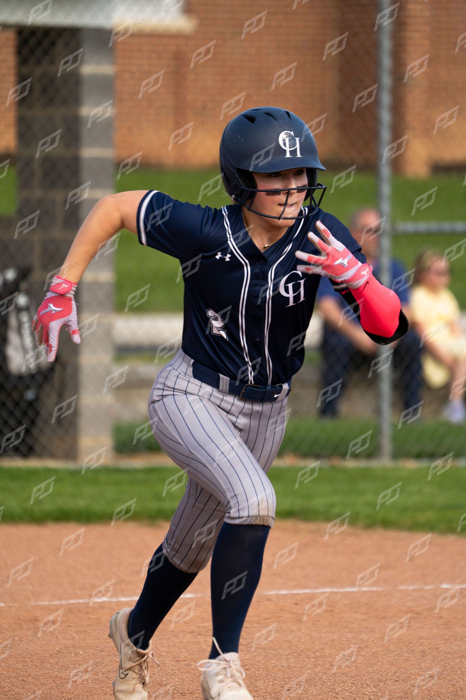 Female softball player in CH navy uniform sprints toward first base during a game.
