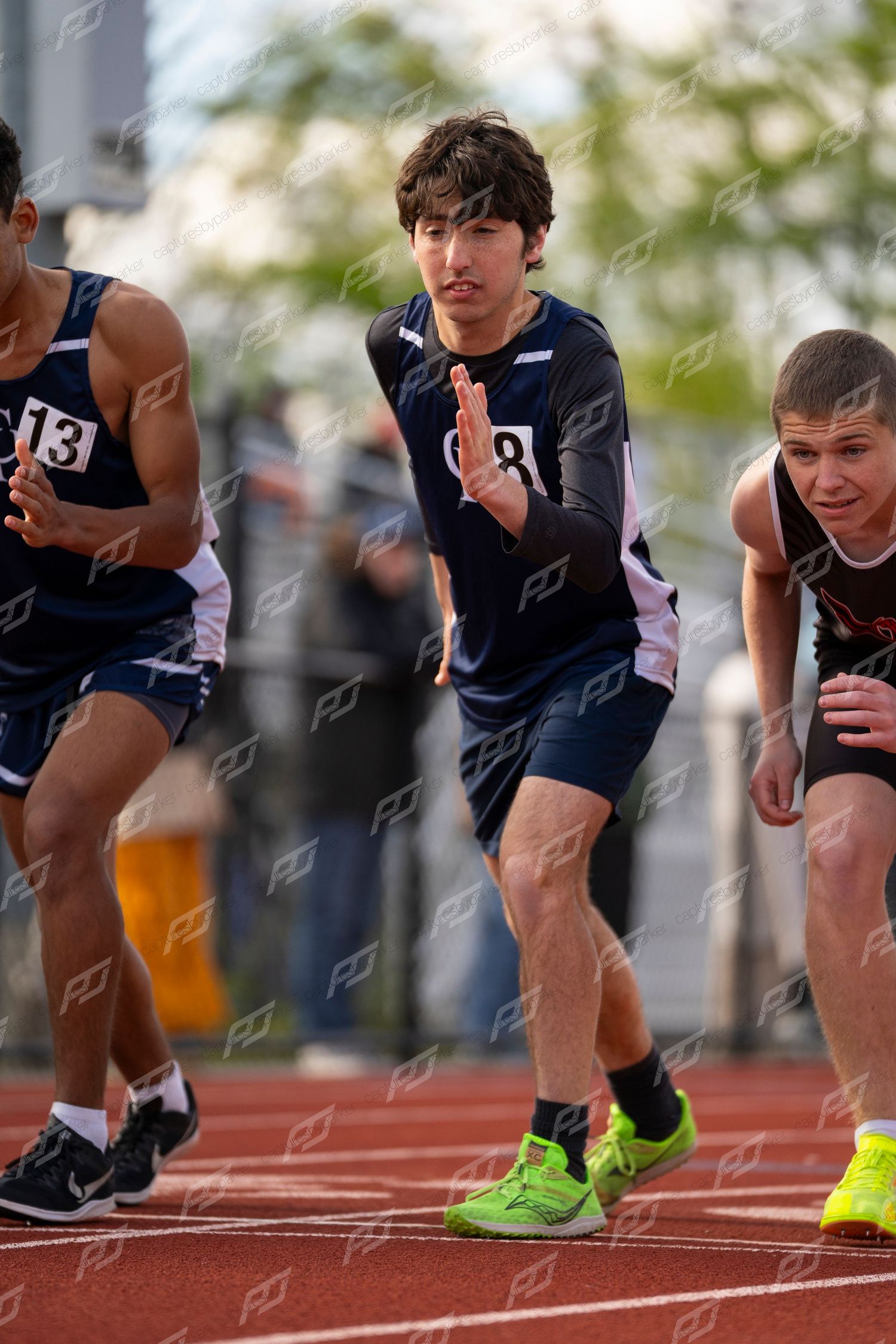 Male sprinter in navy GB uniform bursts forward at start of outdoor track race.