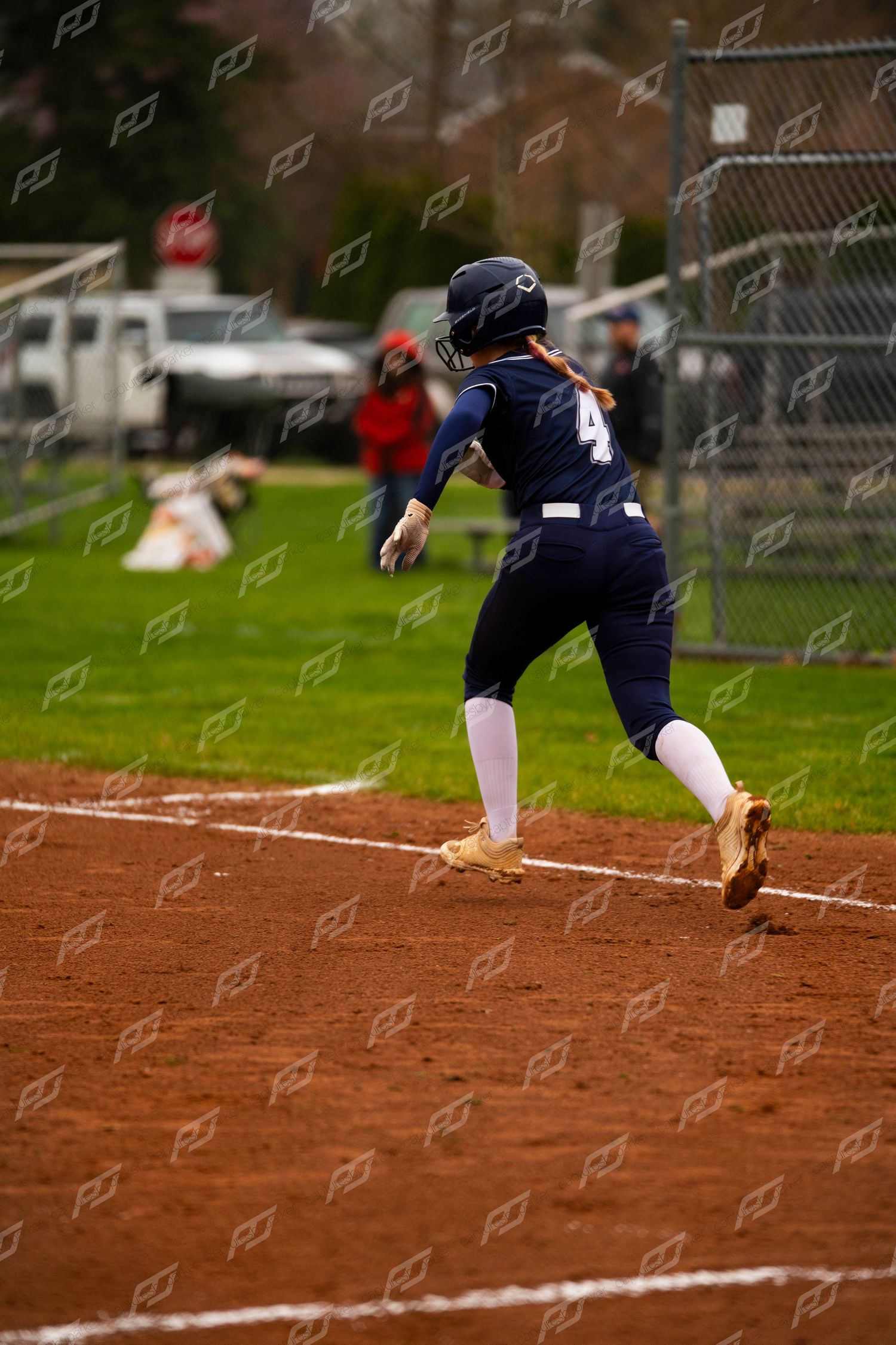 Female softball player #4 in navy uniform sprints along the baseline during a competitive game.