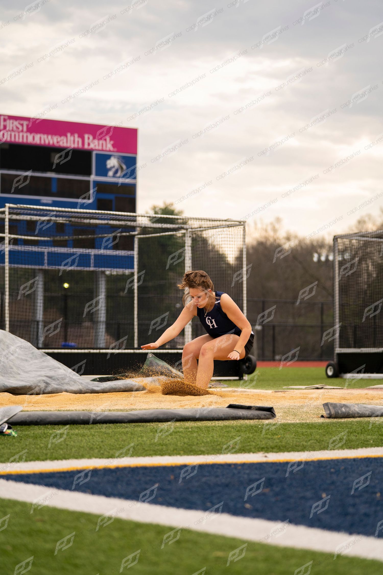 A high school athlete lands in the sand pit during a long jump competition at a track meet.