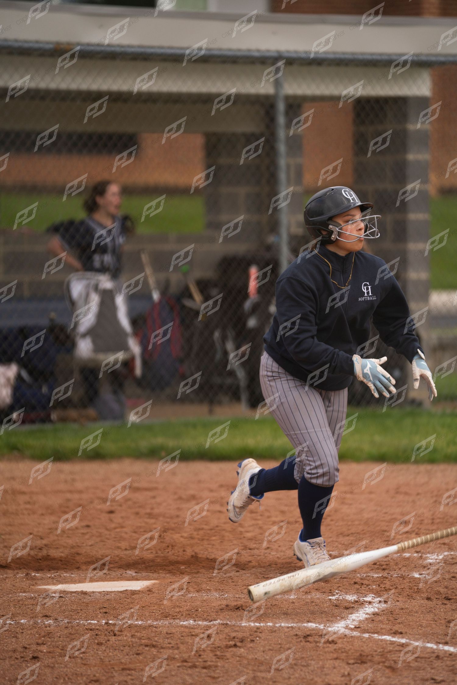 Softball player runs to first base after hitting, wearing navy pinstripe uniform.