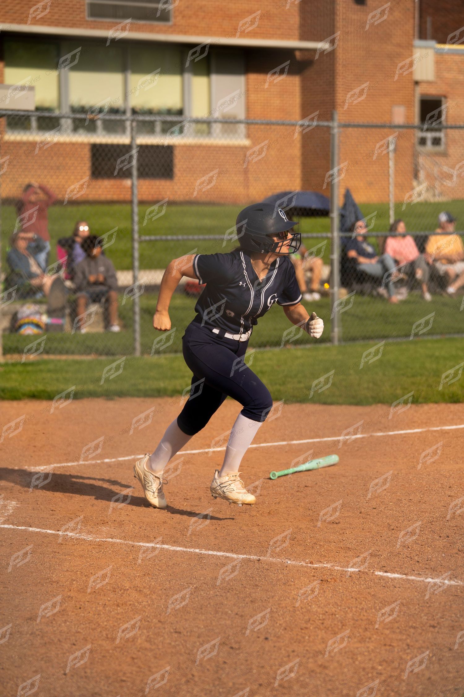 Female softball player sprints toward first base after hitting the ball.