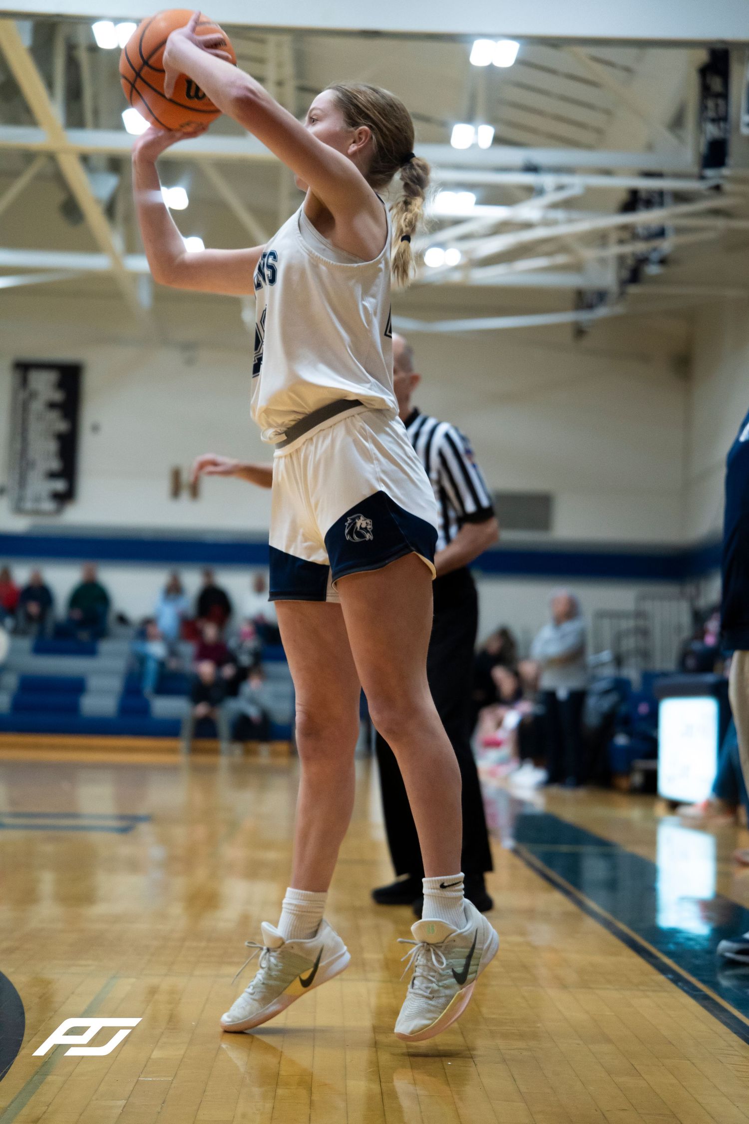 Female Lions basketball player jumps to catch or shoot the ball near the sideline during a high school game.