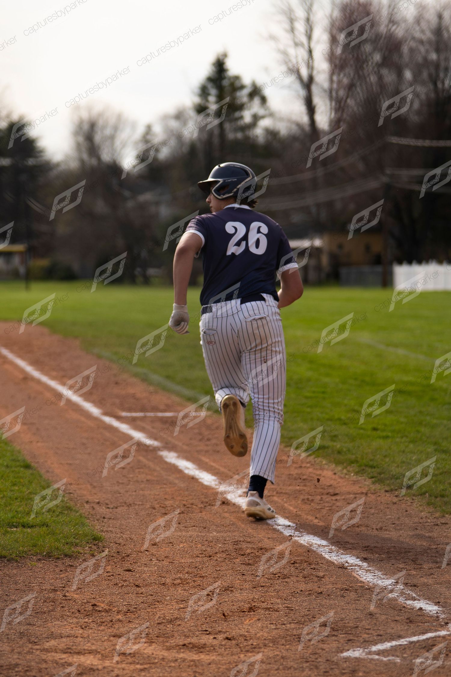 Youth baseball player #26 in navy pinstripe uniform runs along the baseline during a game.